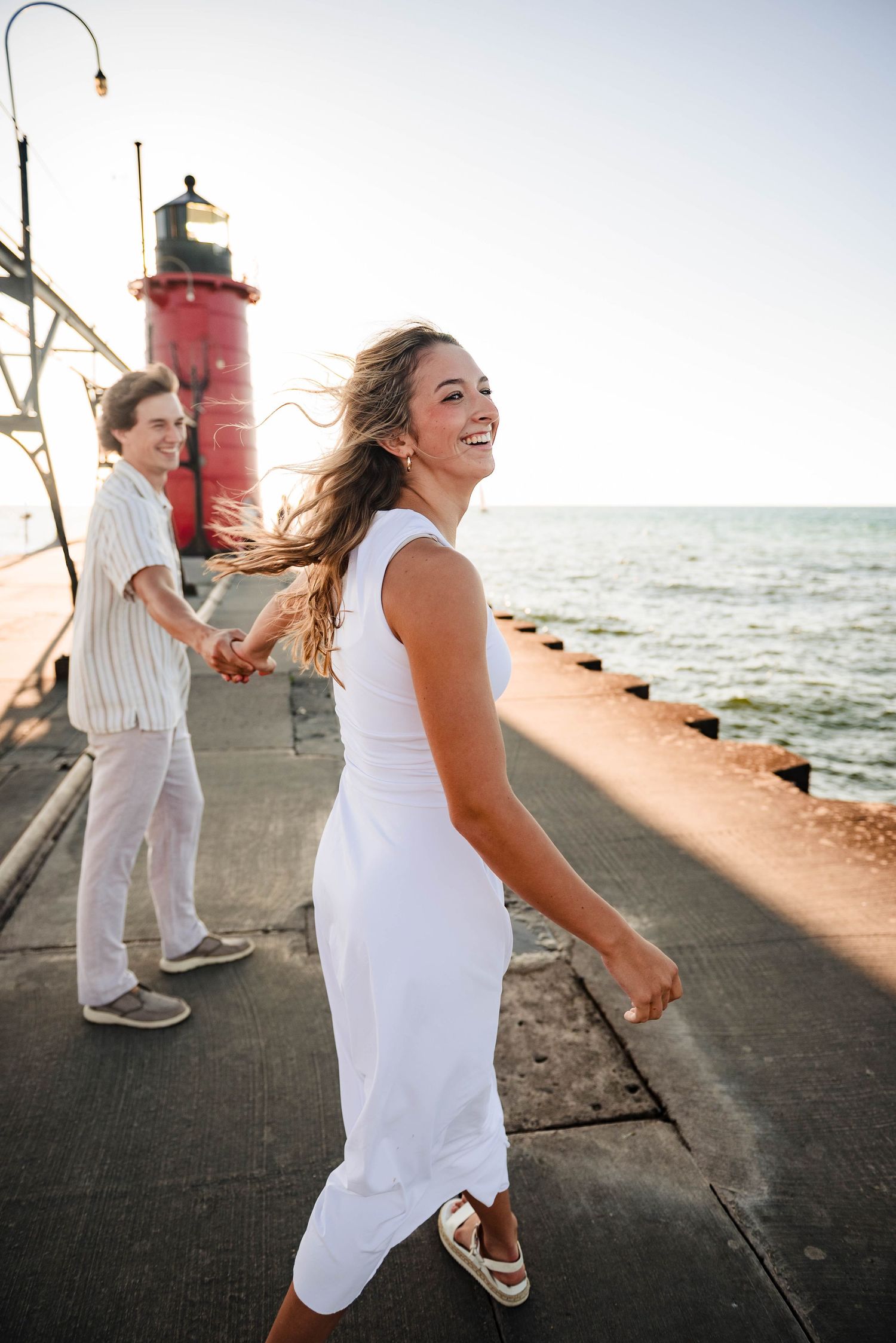 Joyful moment captured on pier with lighthouse and ocean backdrop at sunset.