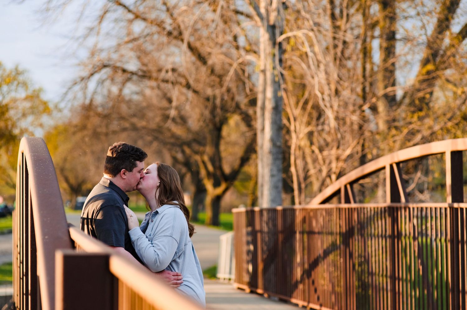 A couple shares an intimate moment on a wooden bridge during sunset.