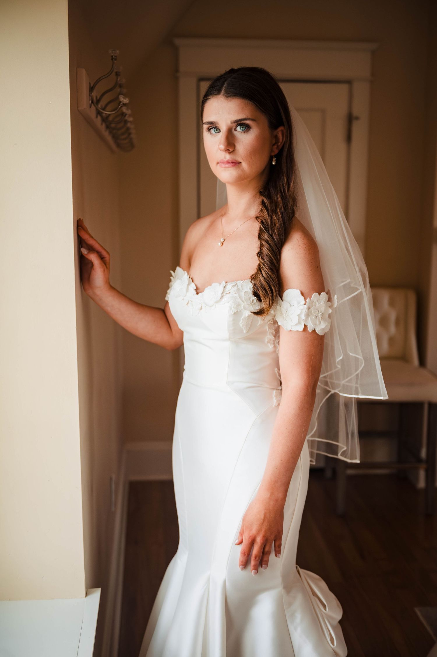Bride in elegant white wedding dress with delicate veil poses indoors.