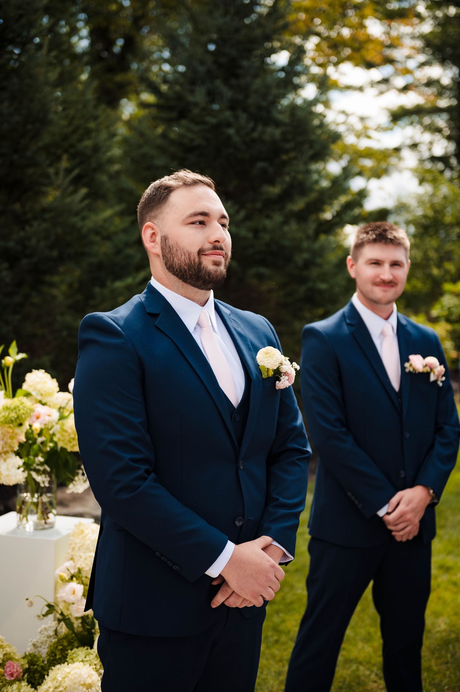 Groomsmen in matching navy suits line up outdoors for wedding photos.