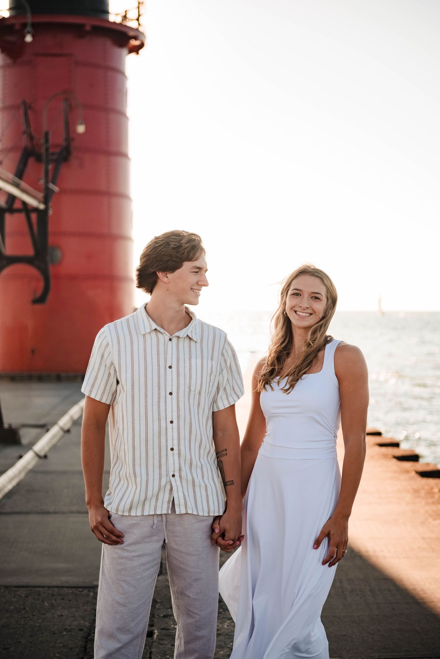 Couple strolls along red lighthouse pier during sunset by the water.