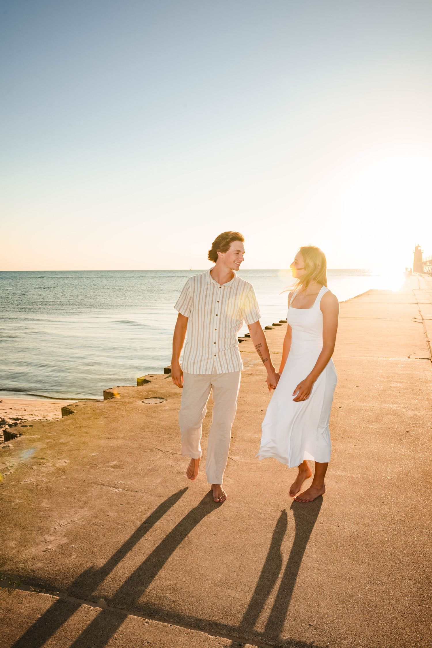 Romantic couple walking on a beach pier during golden sunset casting long shadows.