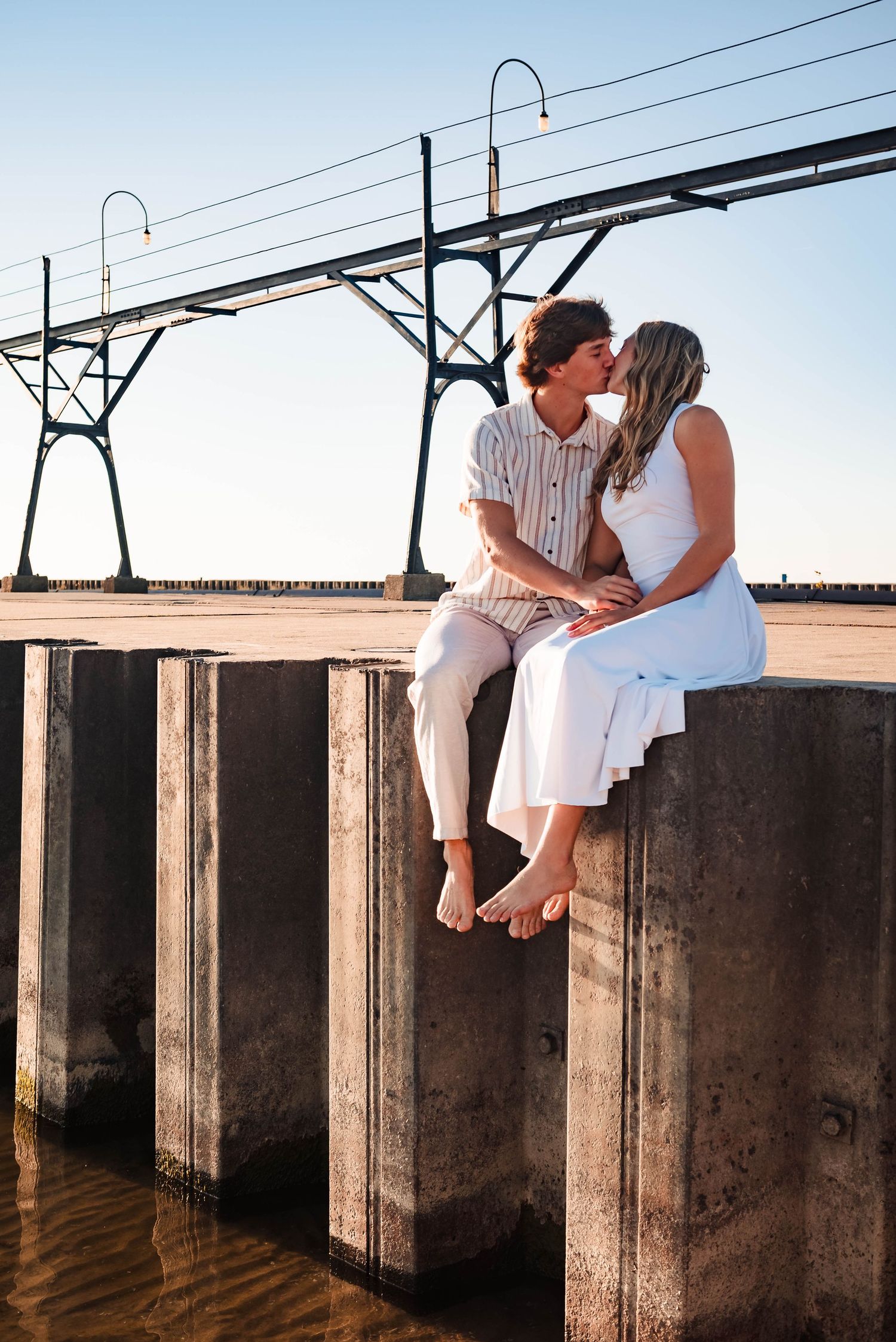 Couple sitting on concrete pier wall sharing intimate moment at sunset.