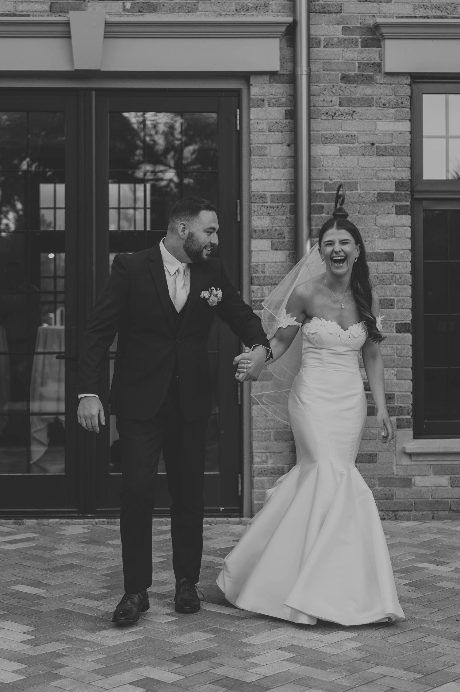 A joyful black and white portrait of newlyweds laughing outside their venue.