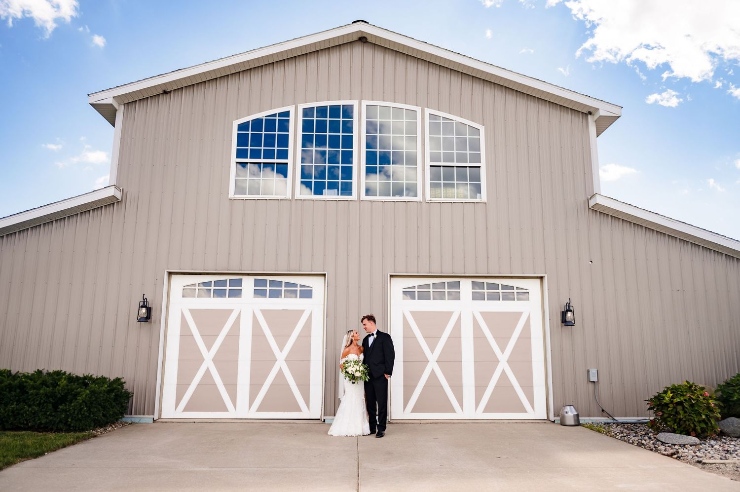 A tan and white barn-style garage door with arched windows and decorative X-patterns is shown against a blue sky.