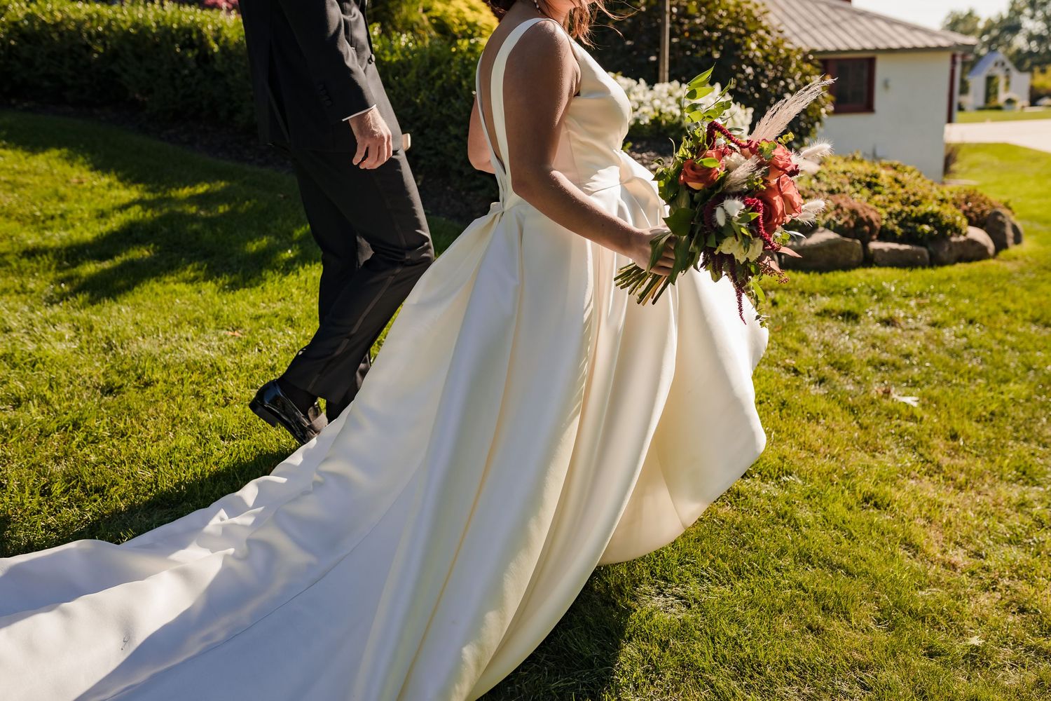Bride in flowing white wedding dress twirls gracefully on a sunlit lawn during an outdoor celebration.