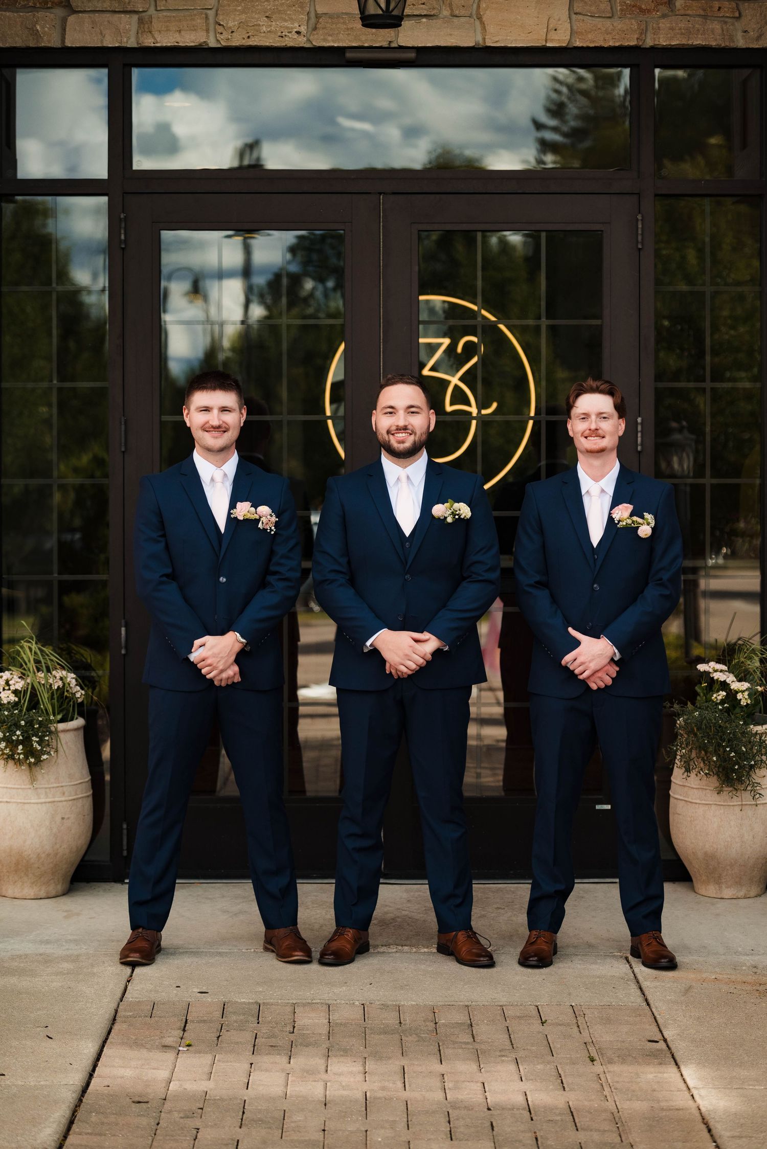 Groomsmen in navy suits pose casually on stone patio outside venue entrance.