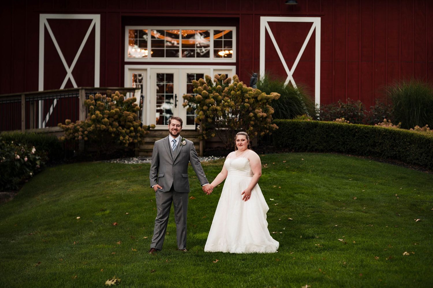 A wedding celebration takes place on a manicured lawn in front of a red barn structure.