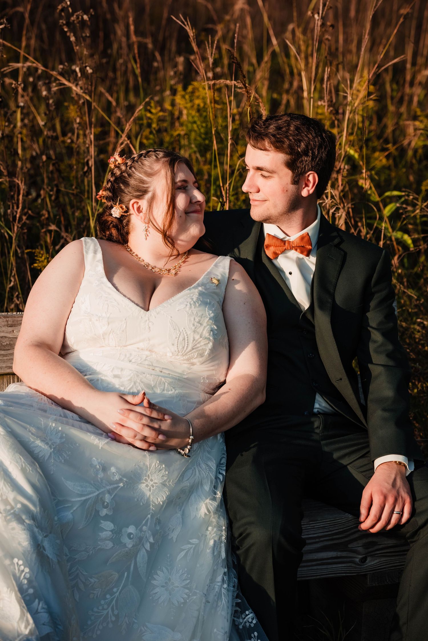 Wedding couple shares intimate moments on rustic wooden bench at sunset.