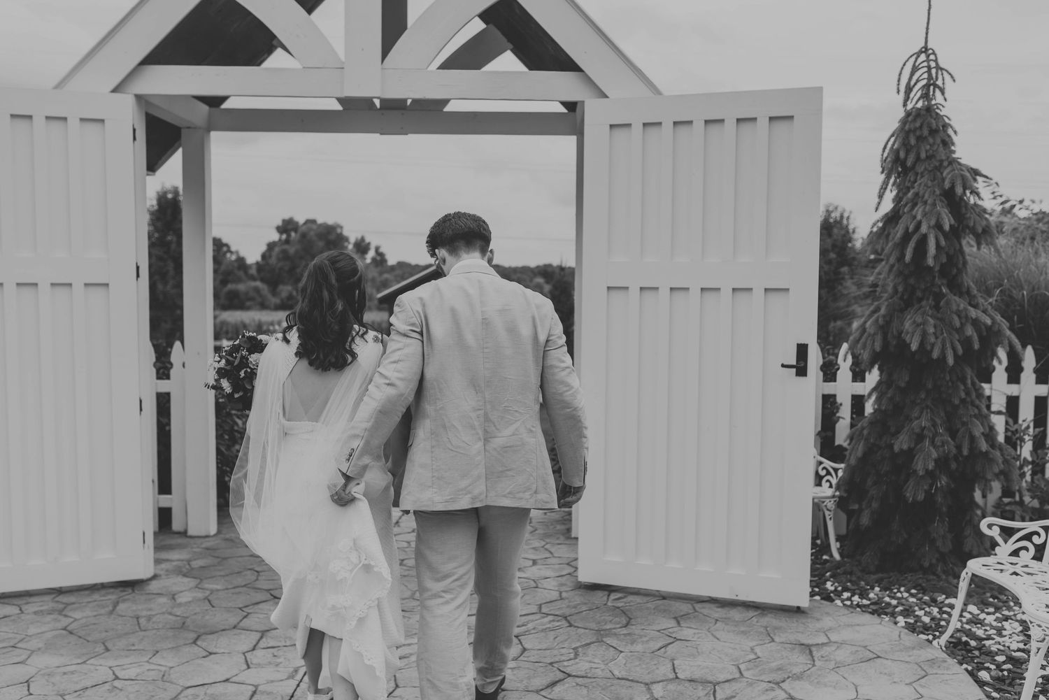 Wedding couple walks along white barn doors in black and white photography.