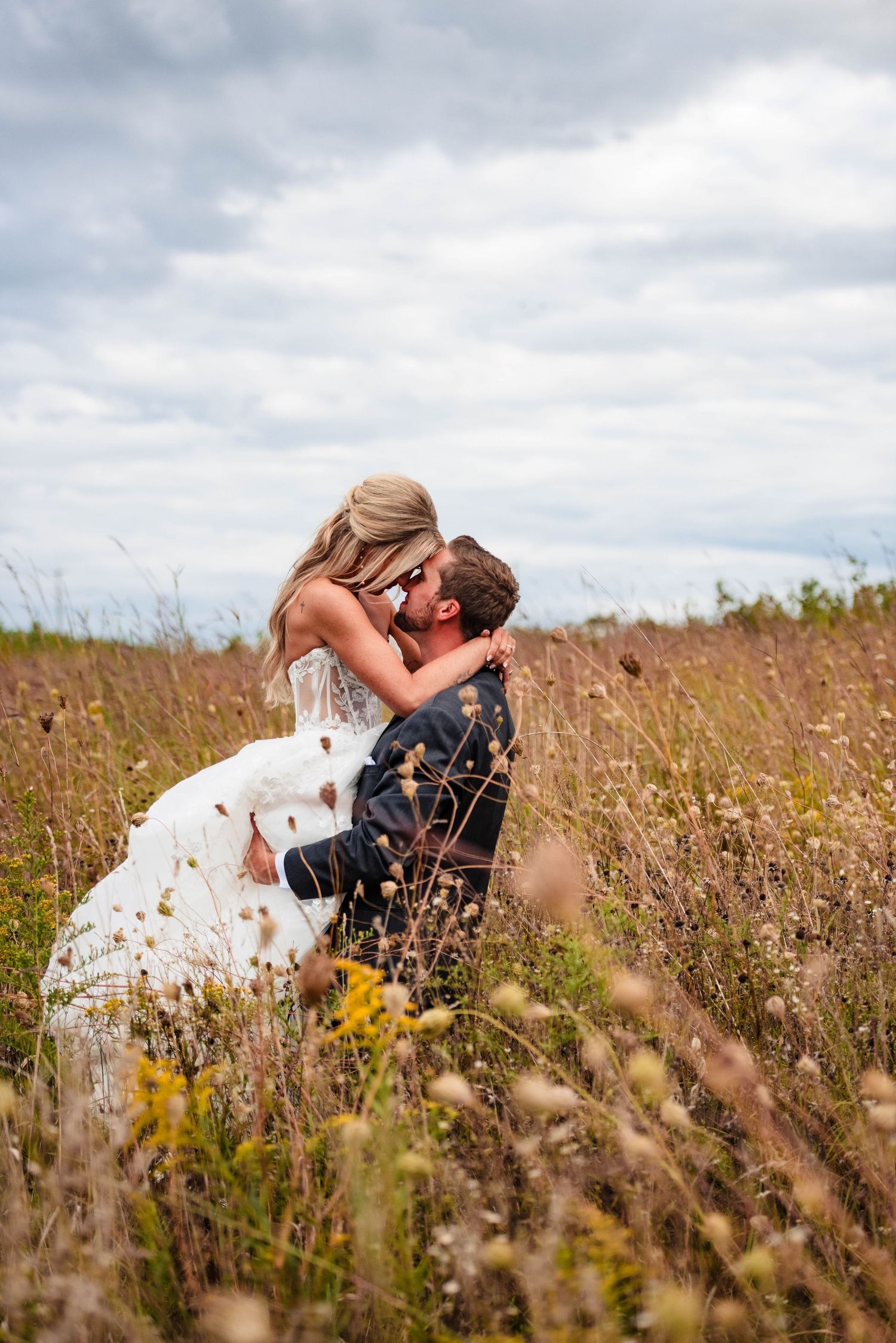 Couple shares romantic kiss in a wildflower meadow with bride's dress flowing in the wind.