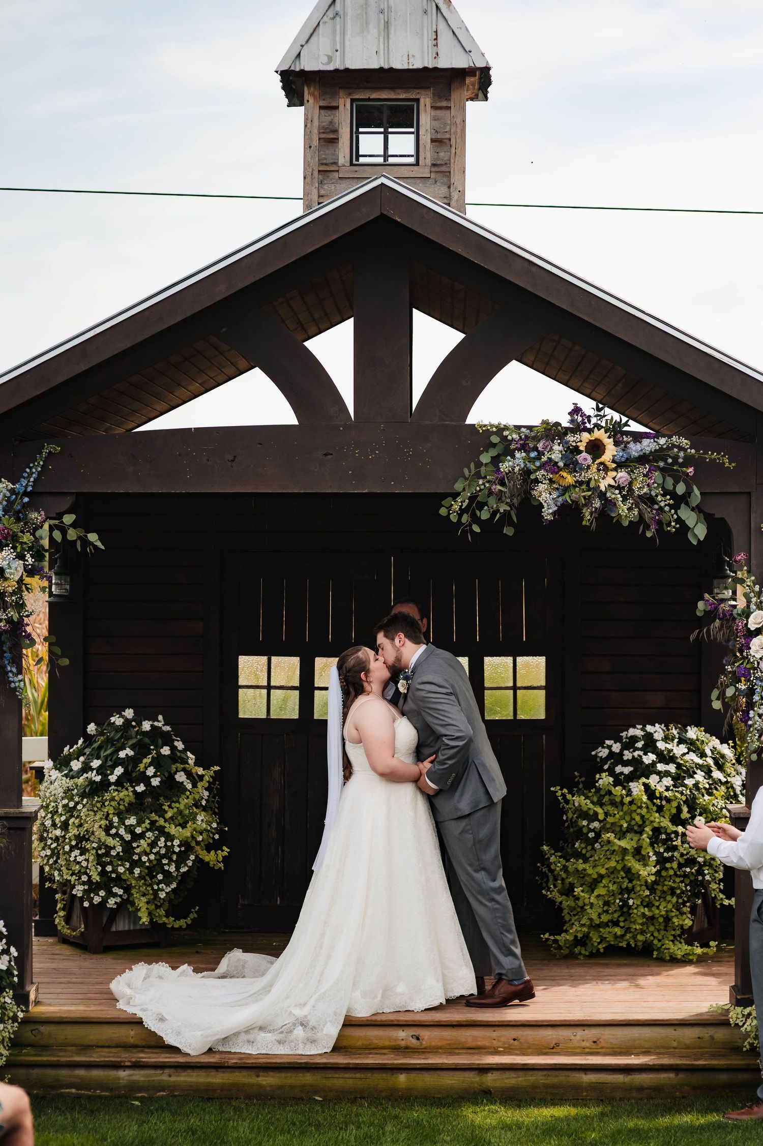 A couple shares romantic moments under a rustic wooden pavilion decorated with floral arrangements.