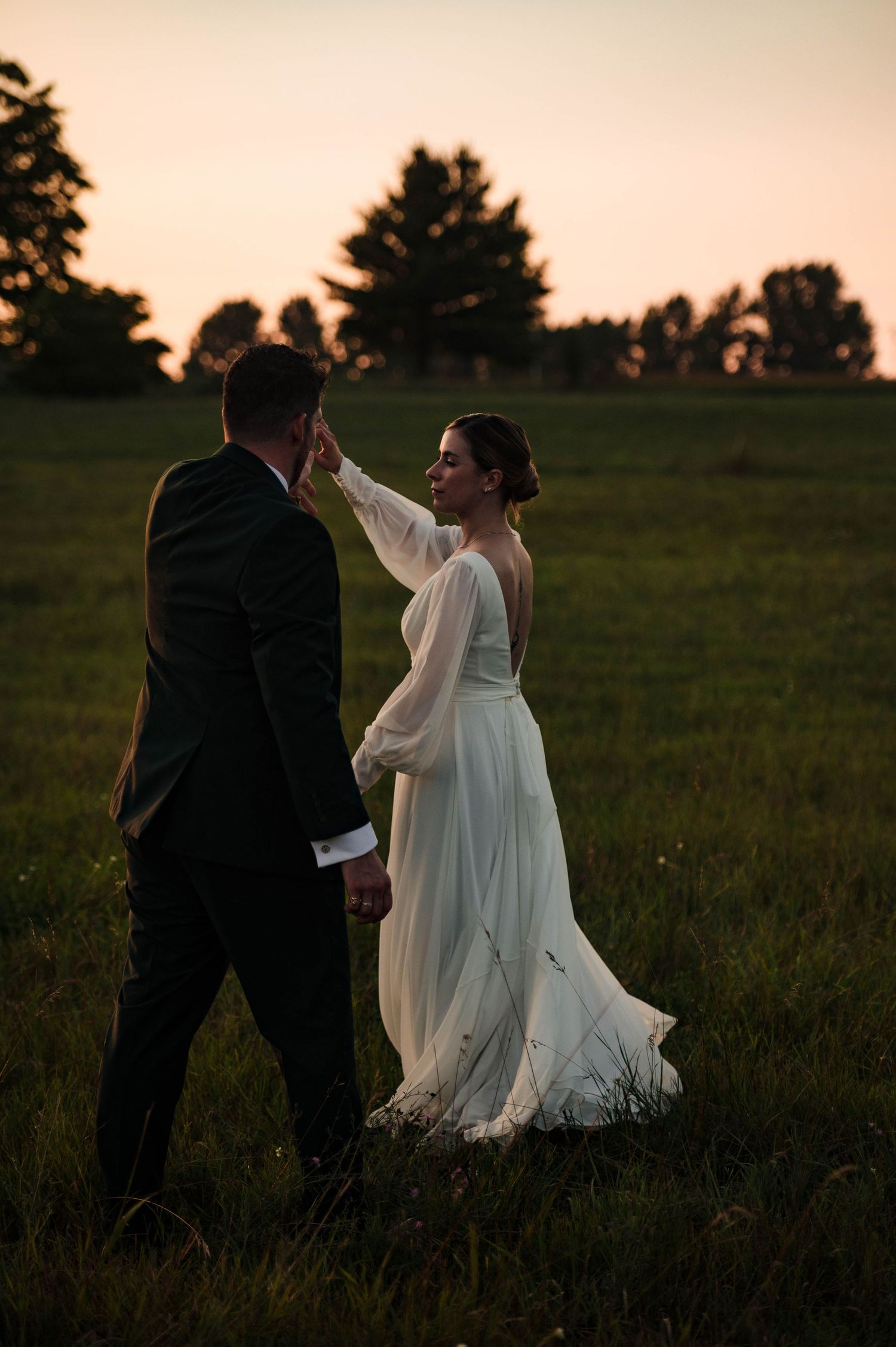Silhouetted couple dances in a meadow during golden hour with dramatic lighting.