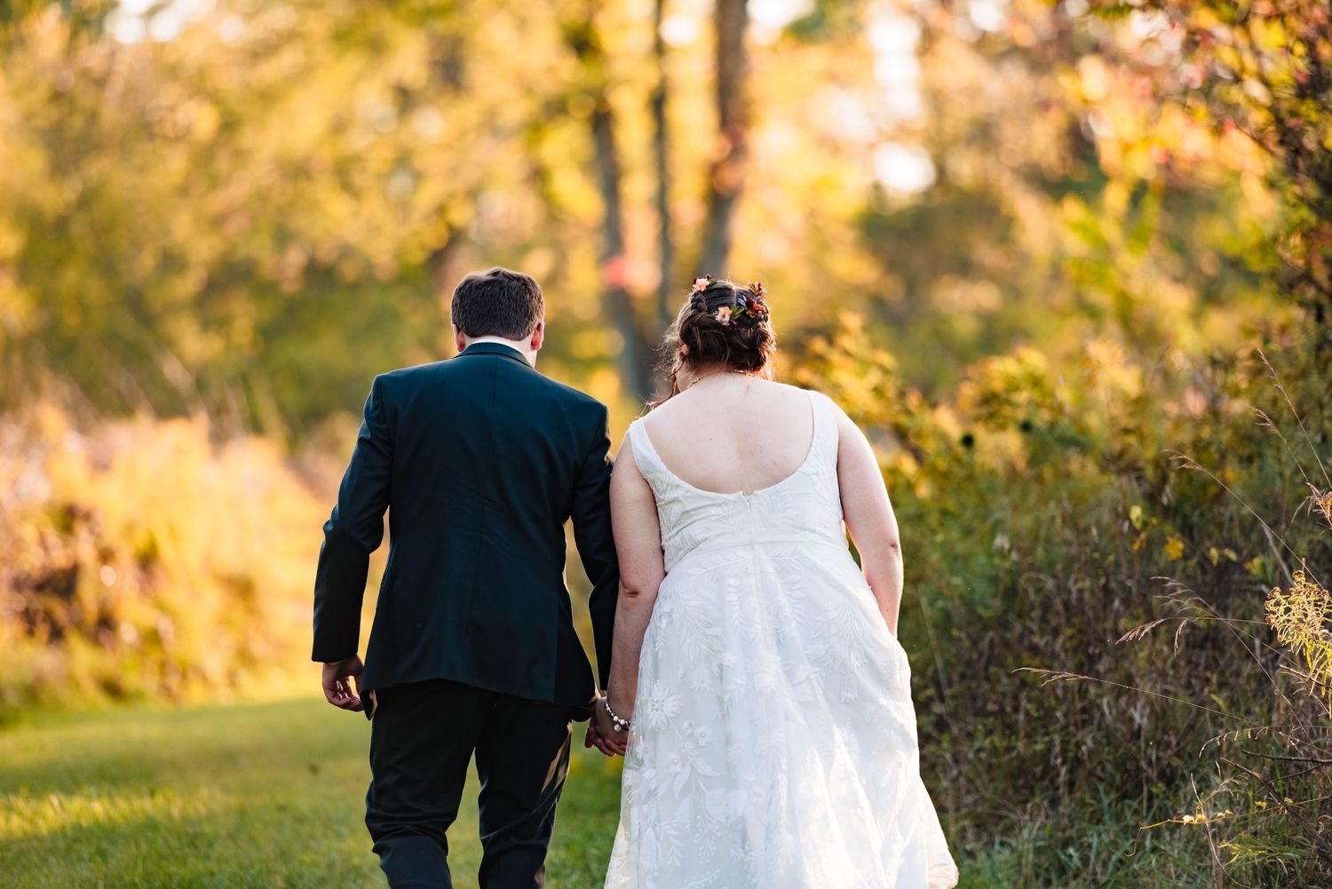 Couple walking together on a sunlit autumn path during their wedding day.