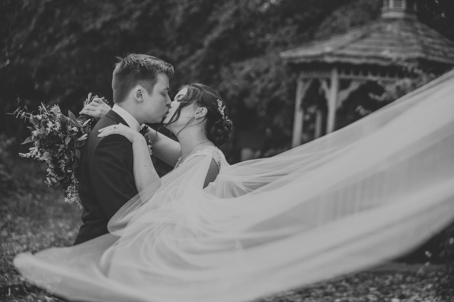 A flowing white wedding veil billows dramatically in the wind during an outdoor photo session.