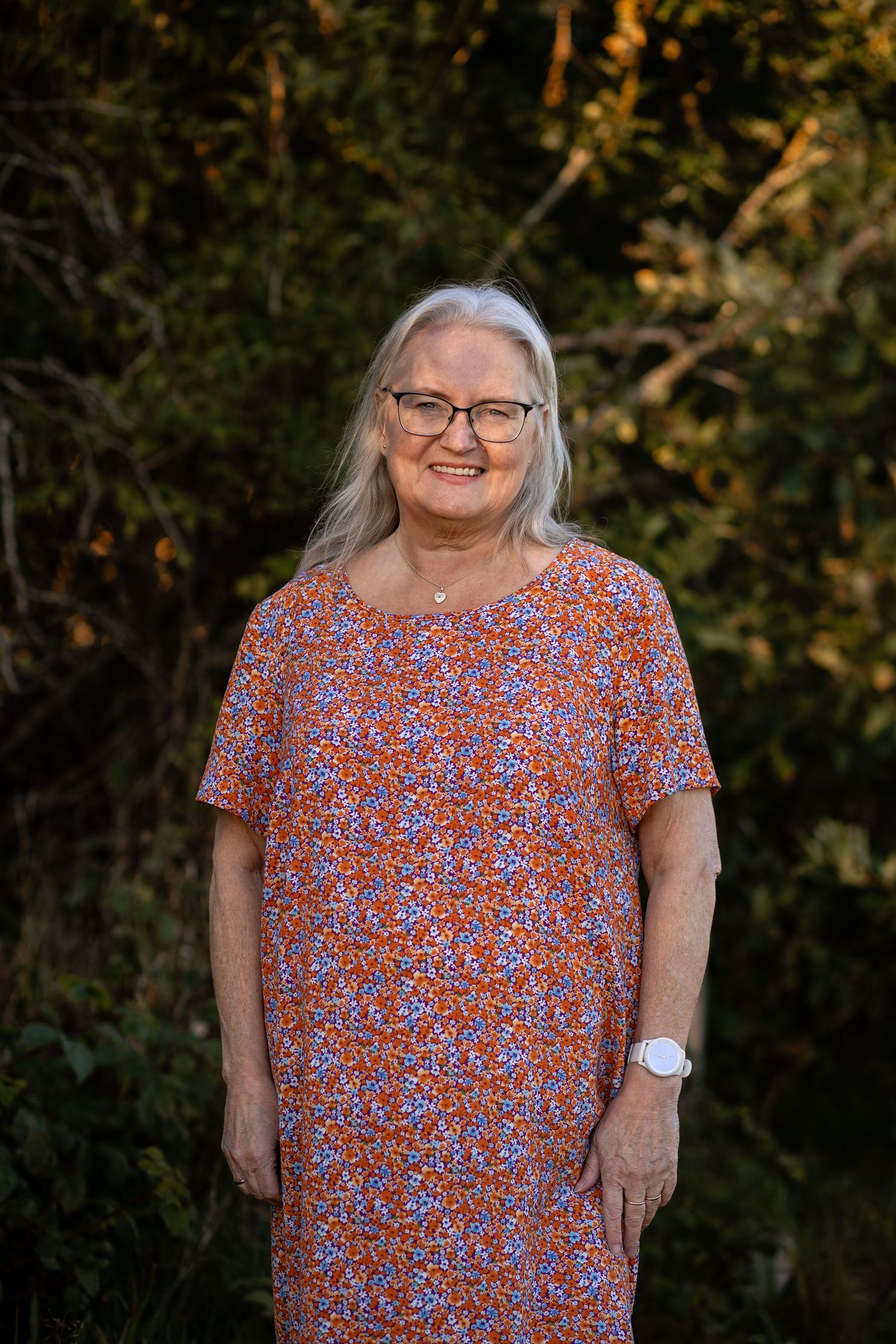 A person in a red floral print dress stands outdoors against a natural background in warm evening light.