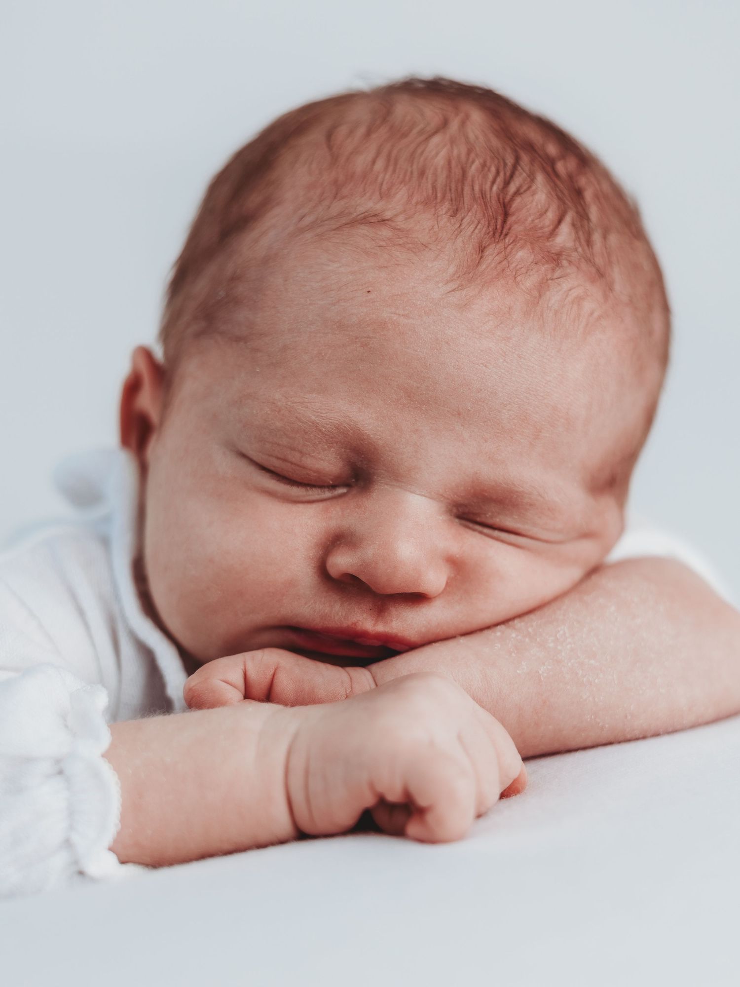 Peaceful sleeping newborn baby in white clothing rests with hands curled up against soft bedding.