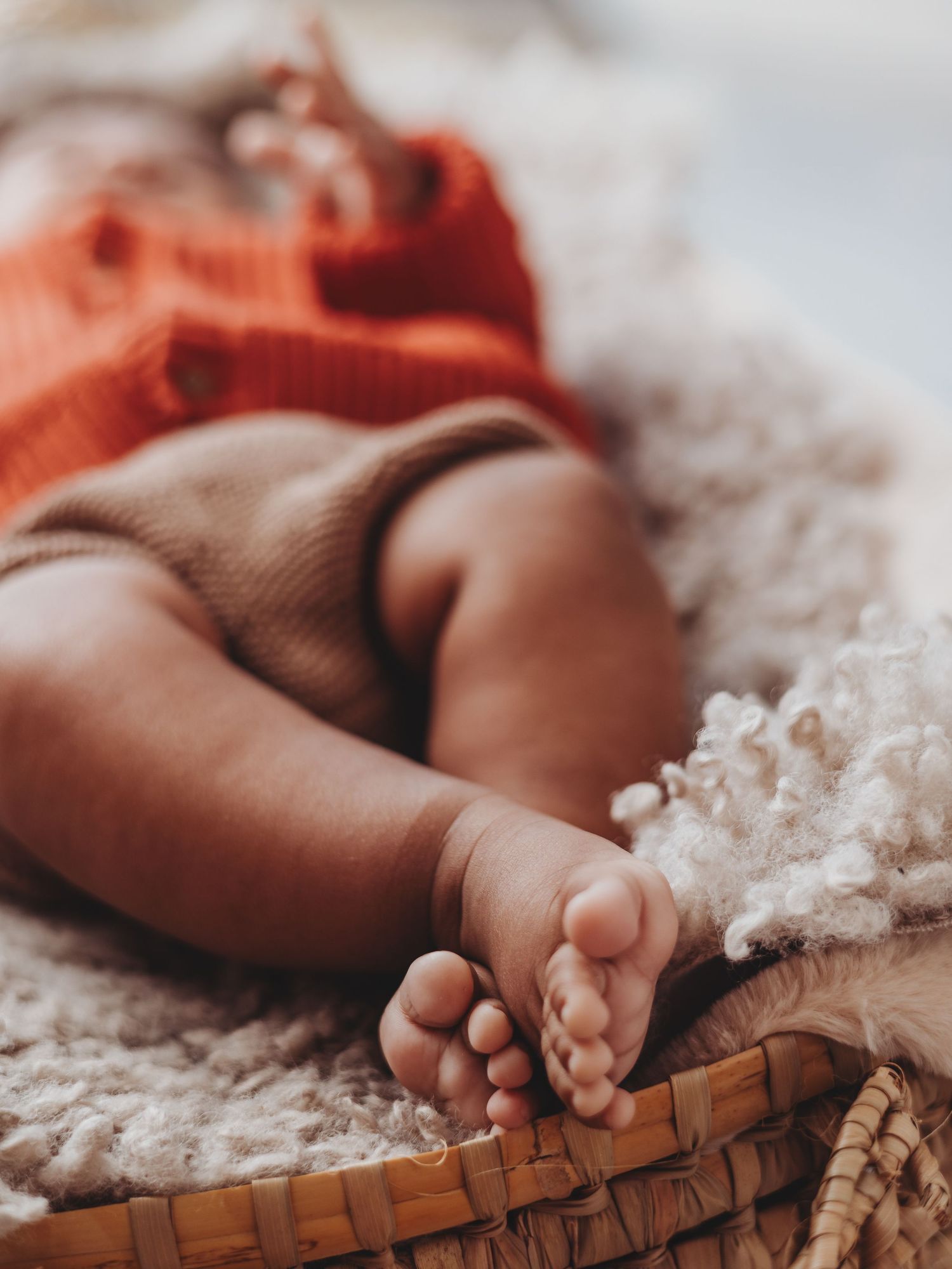 Small baby feet rest gently on a woven basket against soft white cotton fabric in warm lighting.