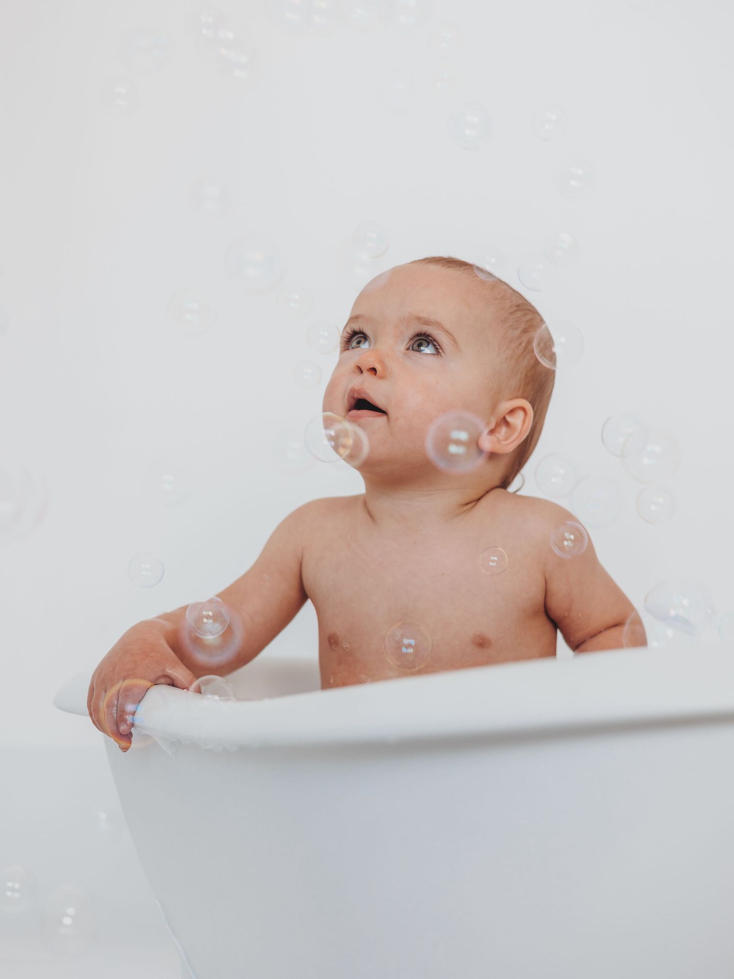A series of minimalist white photos showing a baby looking up at floating soap bubbles in different poses.