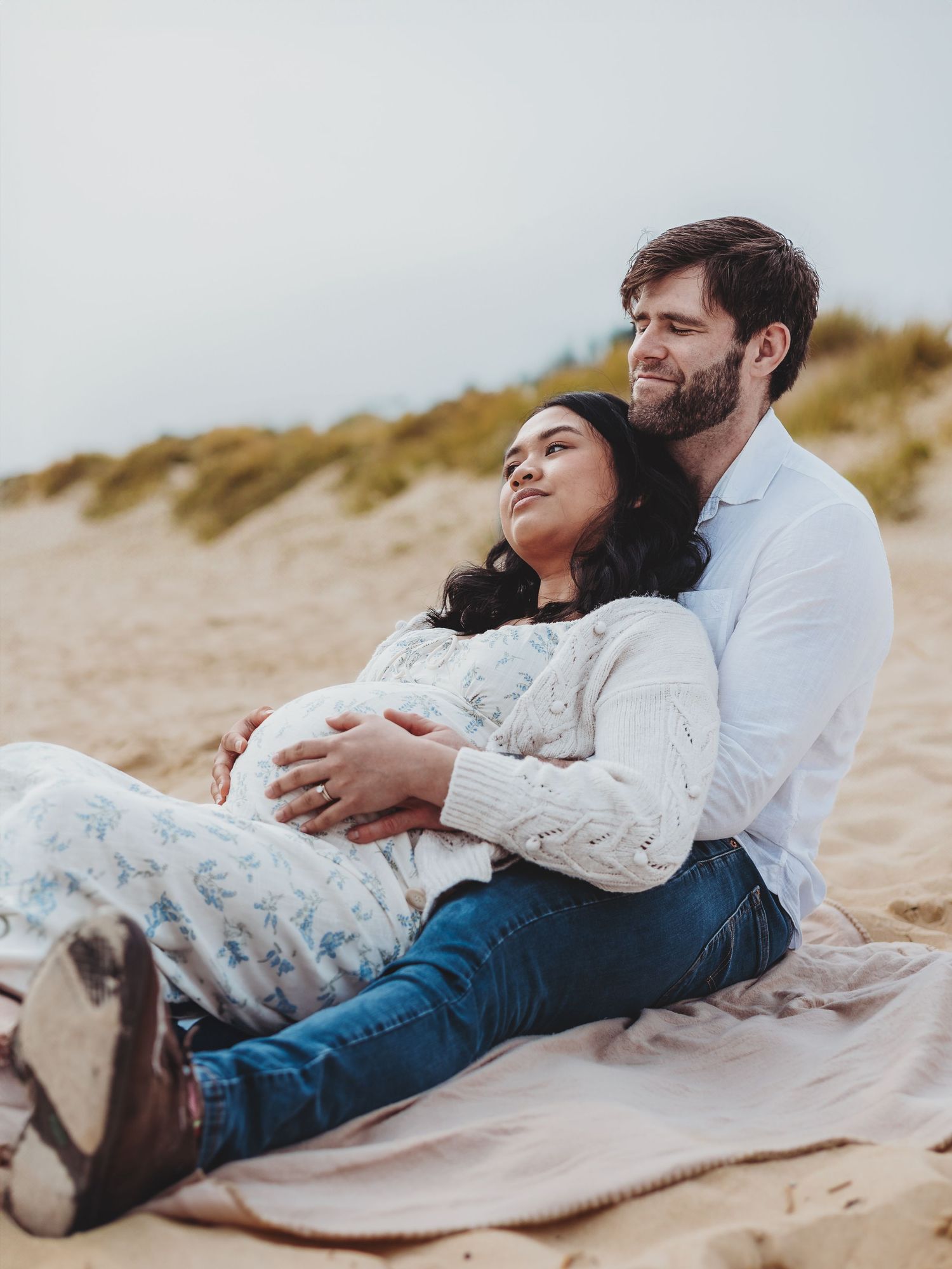 Couple lying together on sandy beach blanket in romantic coastal photoshoot series.