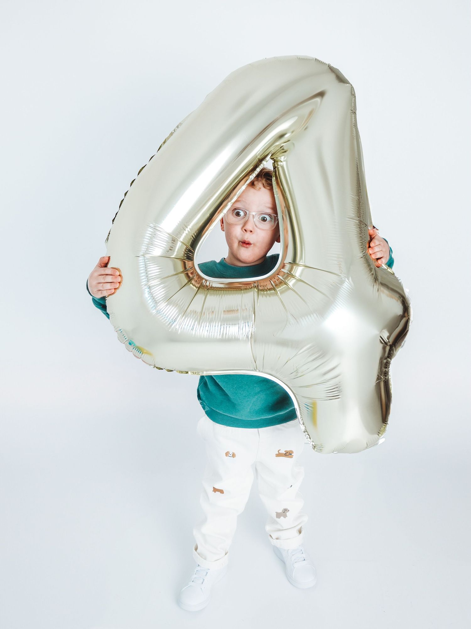 Young child peering through a large gold number 4 balloon, celebrating a 4th birthday party.