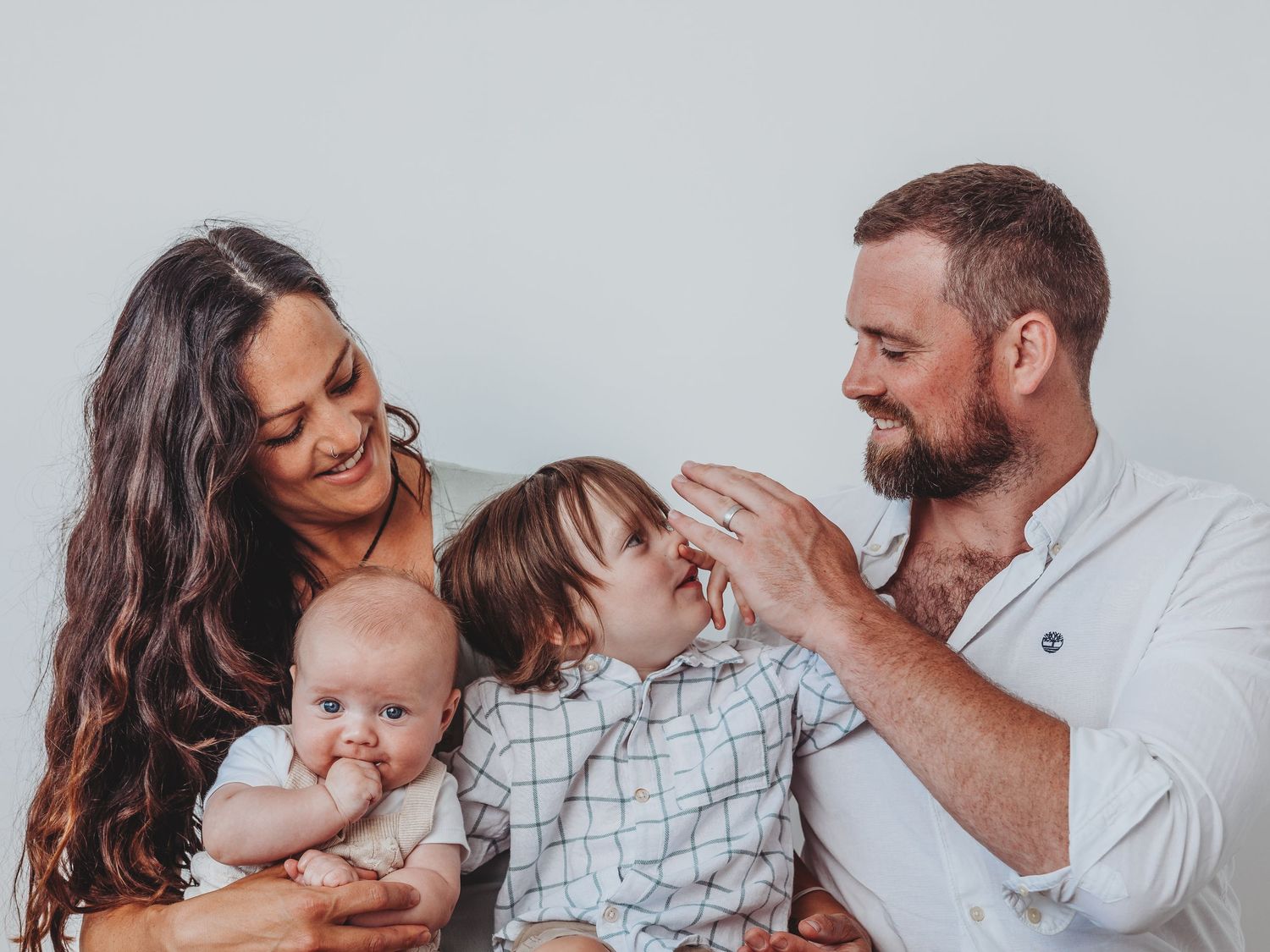 A happy young family with two children, a baby and toddler, sharing a tender moment against a light background.