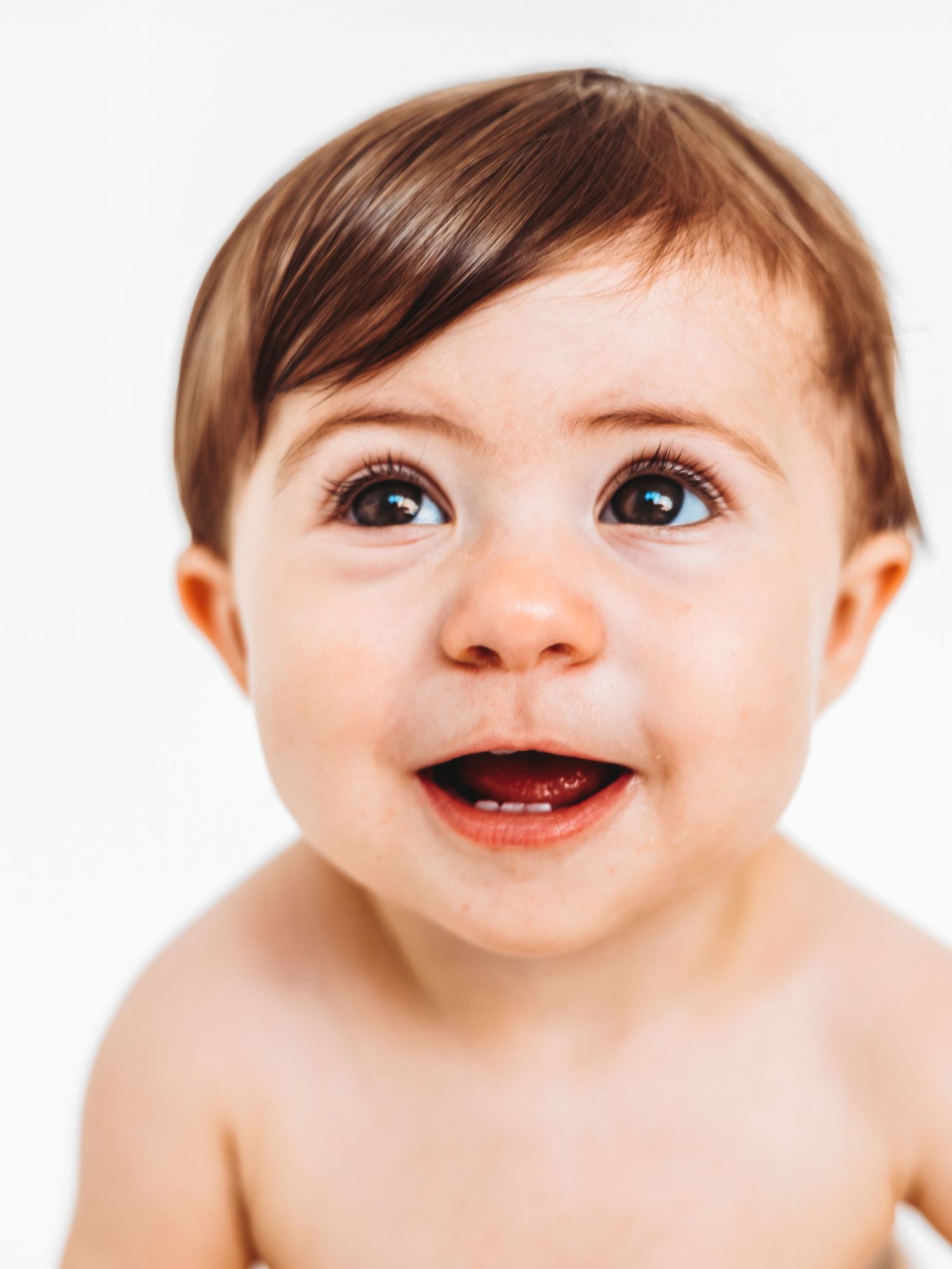 Adorable smiling baby with brown hair and big eyes looking up, portrait on white background.