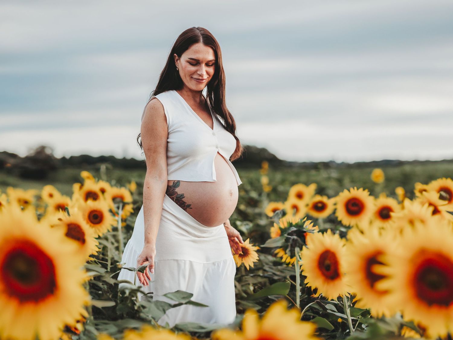 A maternity photo series showing a pregnant woman in a white dress standing in a vibrant sunflower field at sunset.