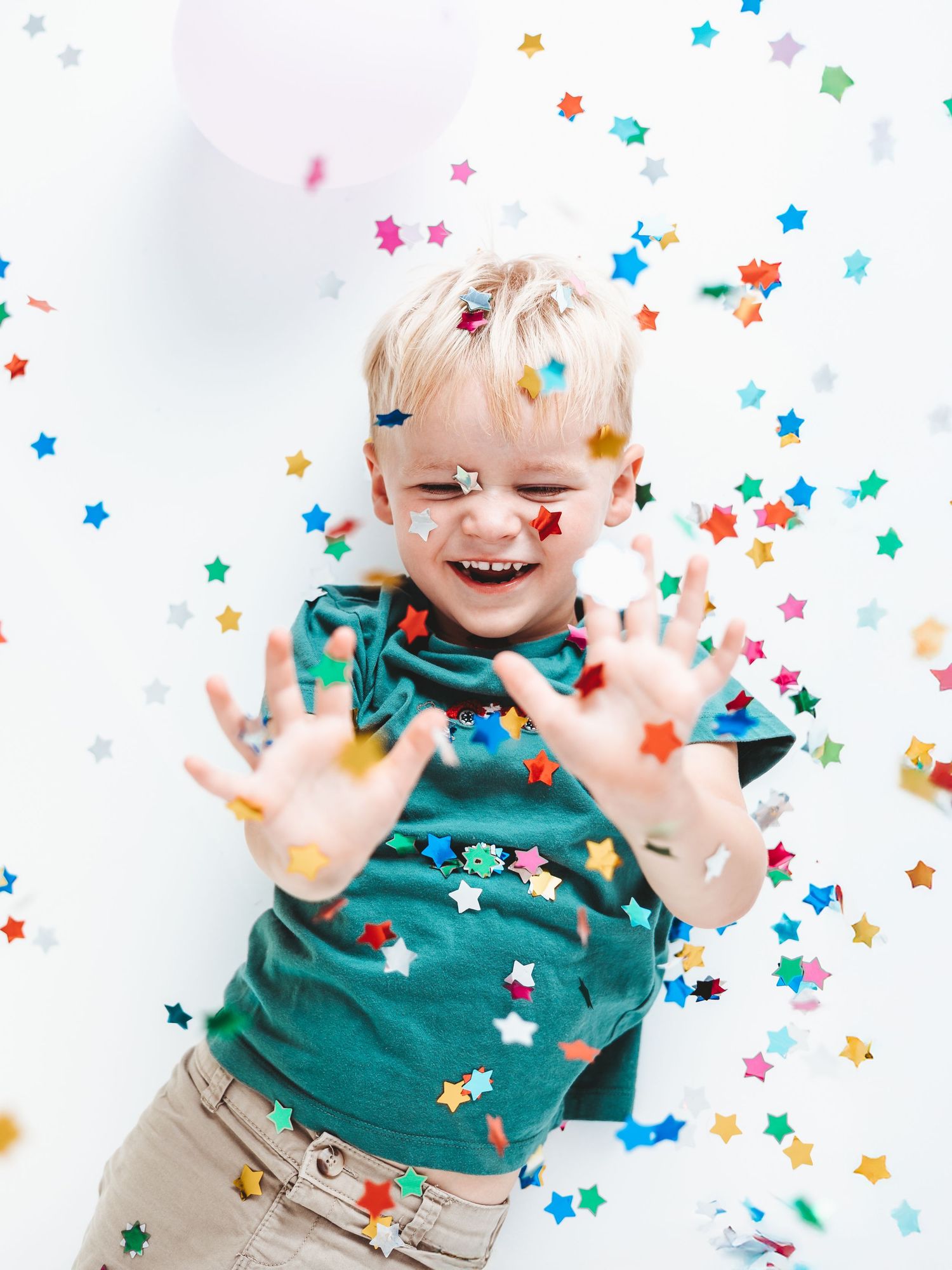 Joyful moment with colourful star confetti falling around a child in a green bow tie. Birthday Photoshoot Dorset.
