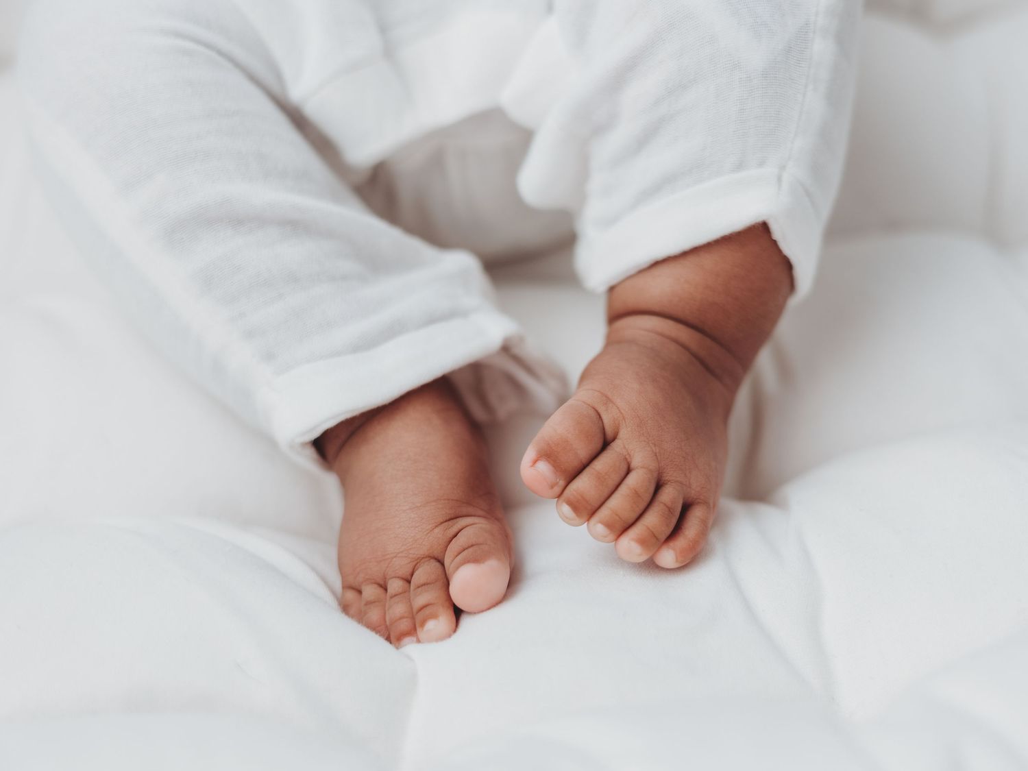 Close-up view of tiny newborn baby feet wrapped in soft white blankets against a light background.
