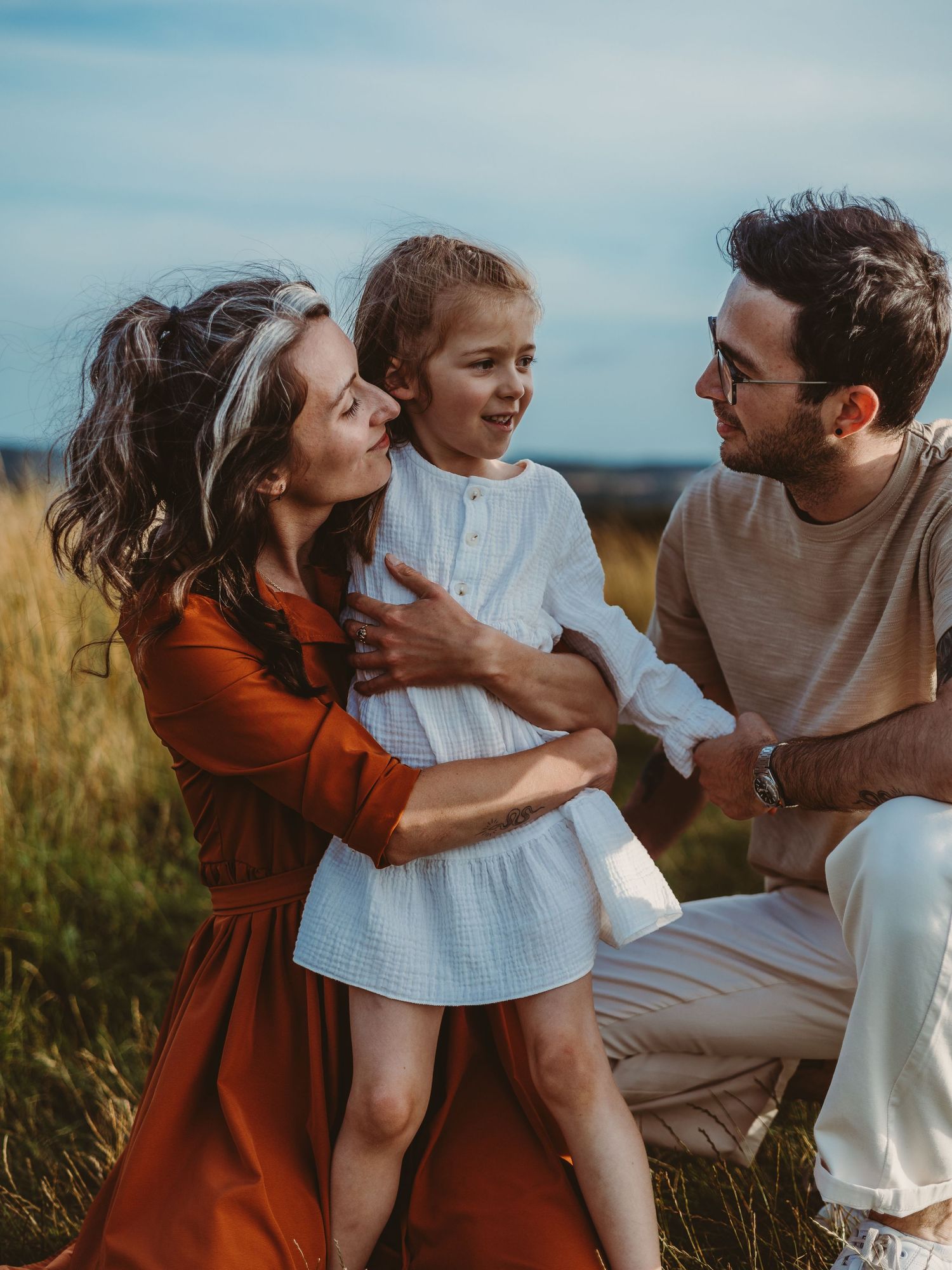 A happy family with a young girl in a white dress enjoying a sunny outdoor moment in a golden field.