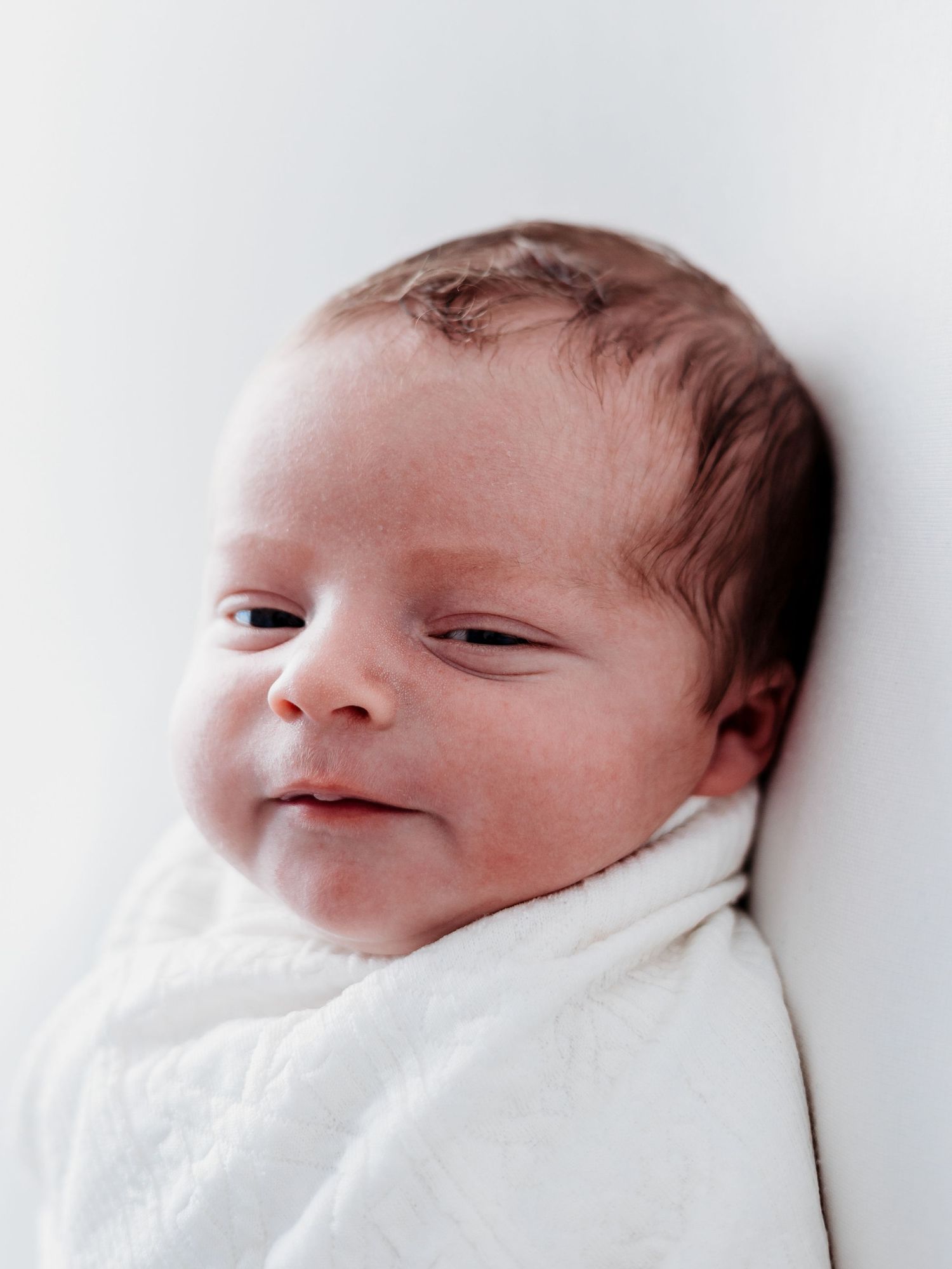 A newborn baby wrapped in white blankets sleeps peacefully in a bright setting.