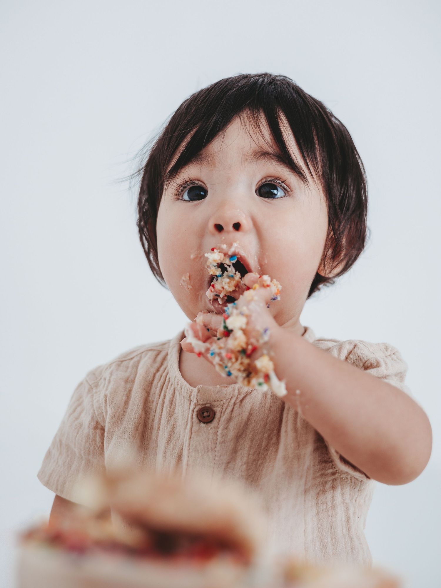 A series of four photos showing a toddler eating cake with messy frosting all over their mouth and fingers.