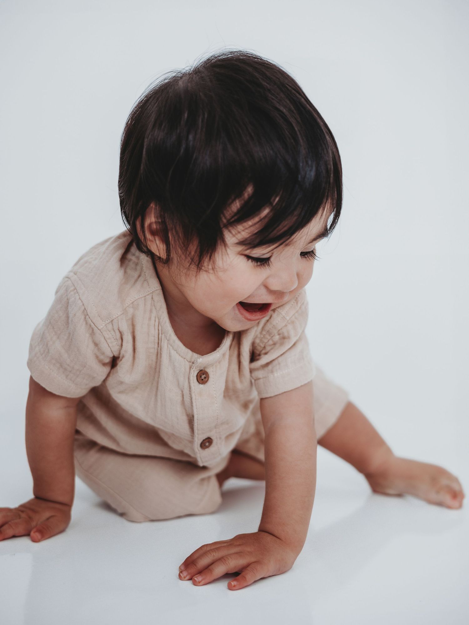 A baby in beige clothing crawls and moves across a white background in a series of progressive motion shots.
