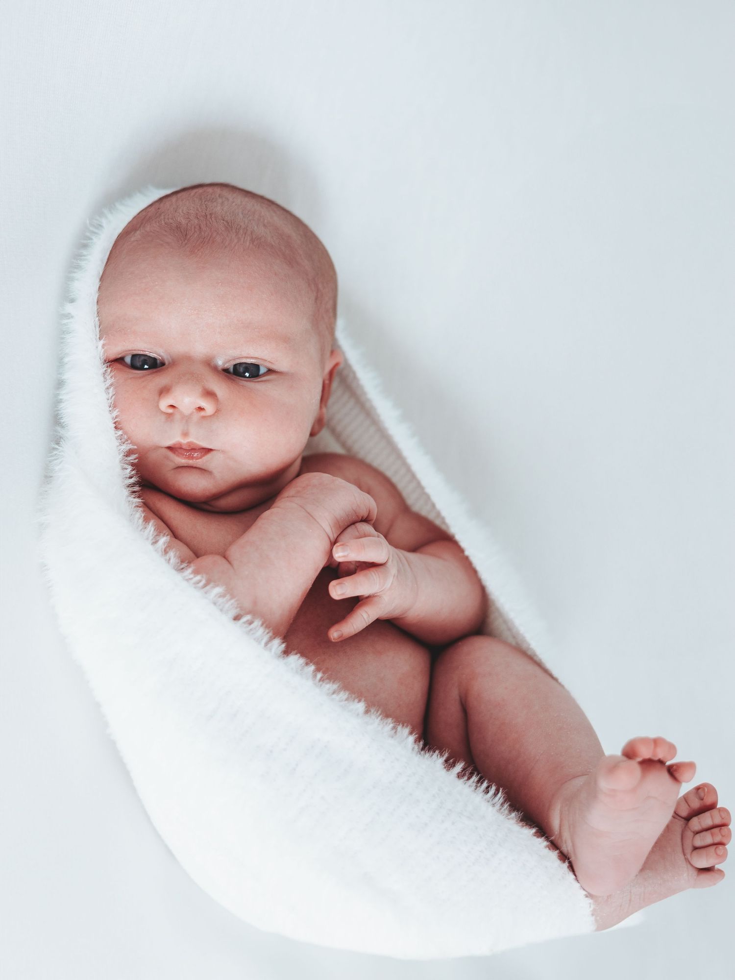 A series of five photos showing a newborn baby wrapped in white blankets with different expressions and poses.