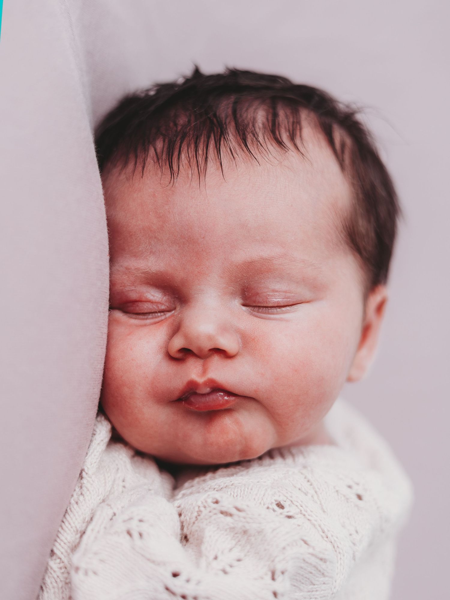 A sleeping newborn baby wearing white lace clothing is shown in a series of peaceful close-up portraits.