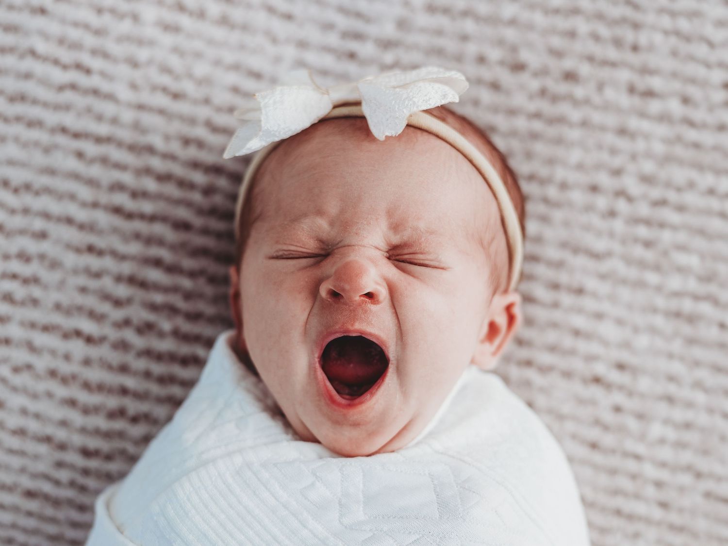 Baby in white outfit lying on textured beige blanket shown from various angles.