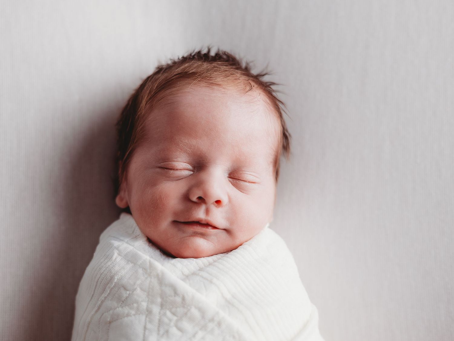 A peaceful sleeping newborn baby wearing white against a light gray background.