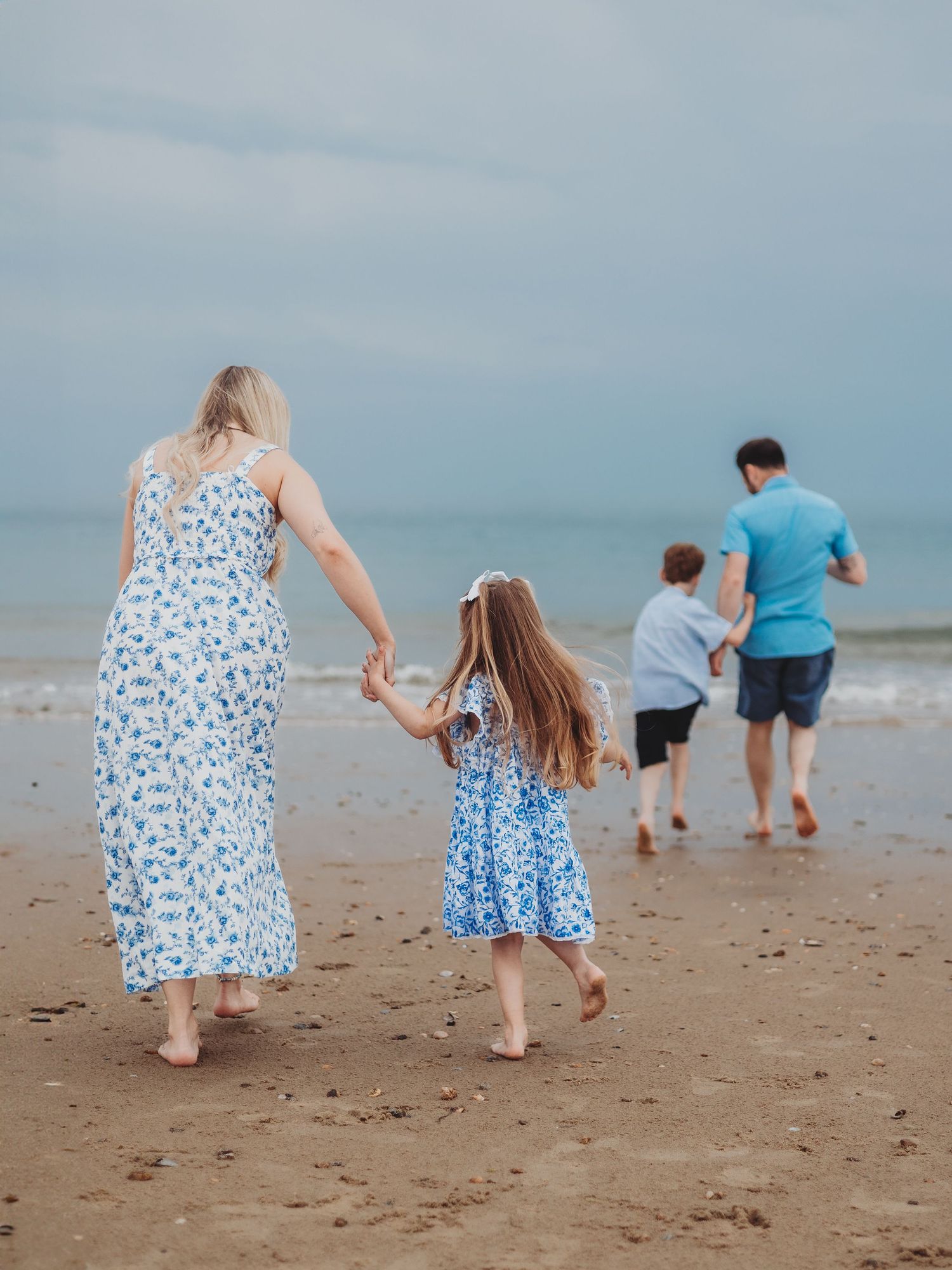 Family walking hand-in-hand on a sandy beach, wearing matching blue floral outfits, with ocean waves in the background.