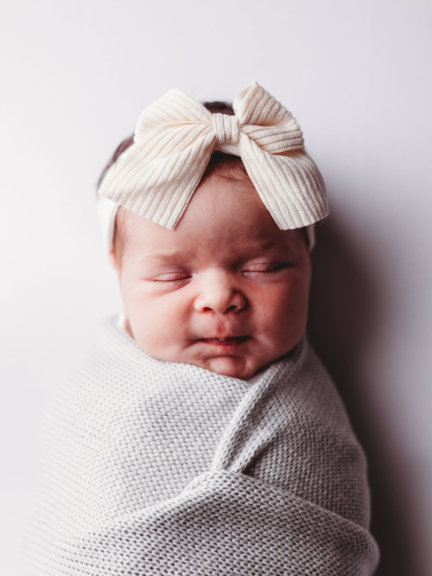 A sleeping newborn swaddled in gray fabric wearing a striped bow headband on a white background.