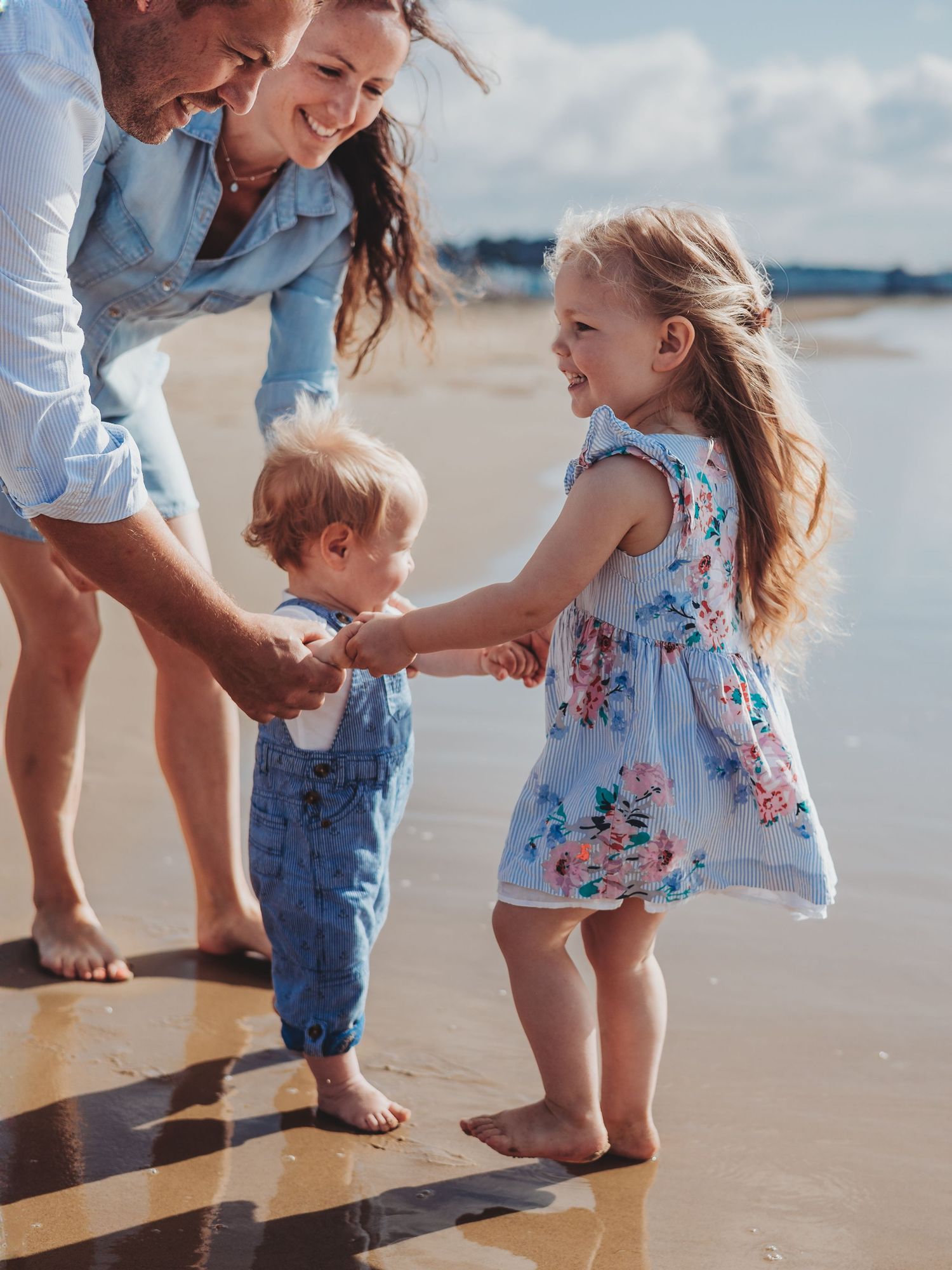 Family with two young children playing barefoot on a sandy beach on a sunny day.
