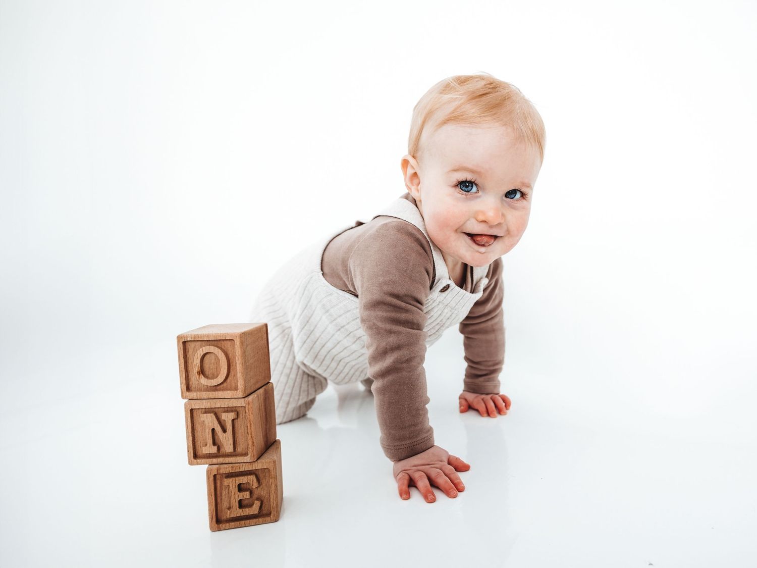 Baby crawling next to stacked wooden alphabet blocks spelling ONE on a white background.