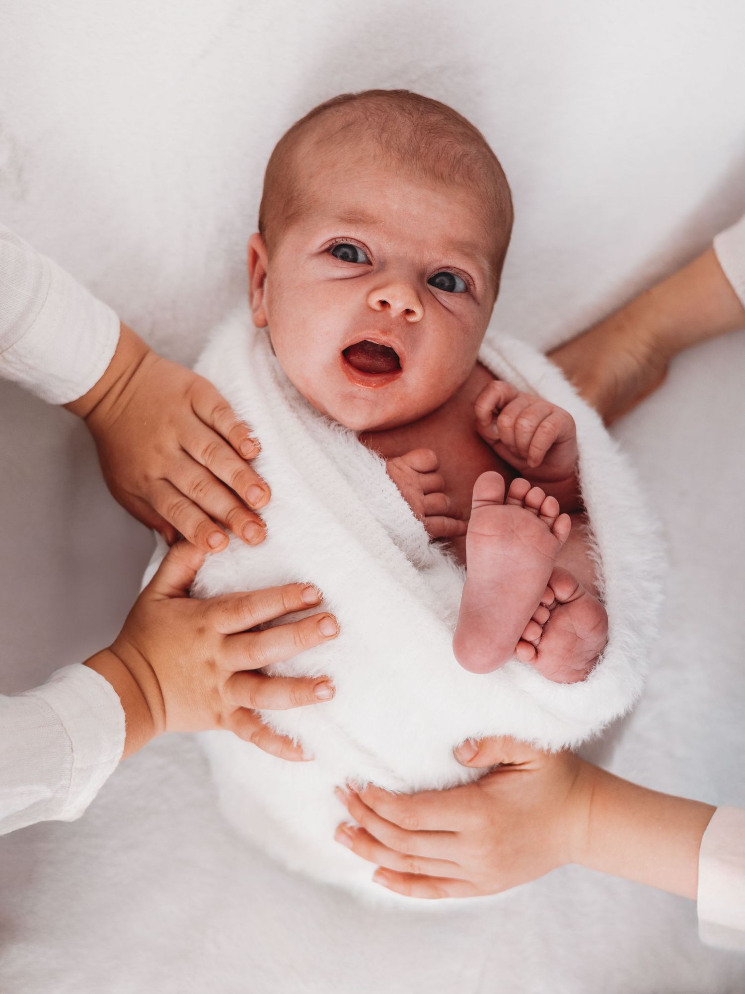 A newborn baby being gently wrapped in a soft white towel during bath time, showing multiple stages of drying.