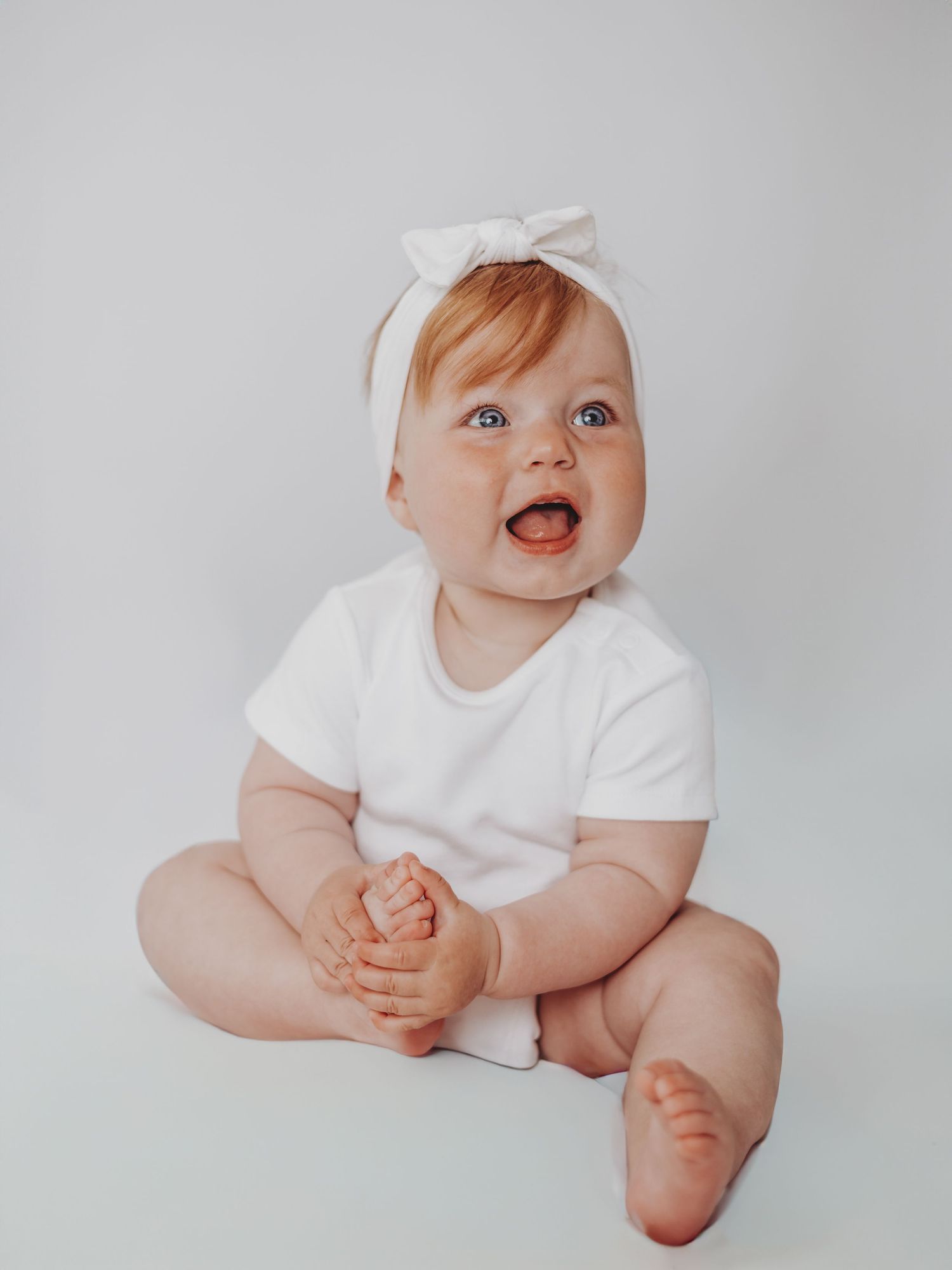 A series of four minimalist studio portraits showing a baby in a white onesie against a light gray background.