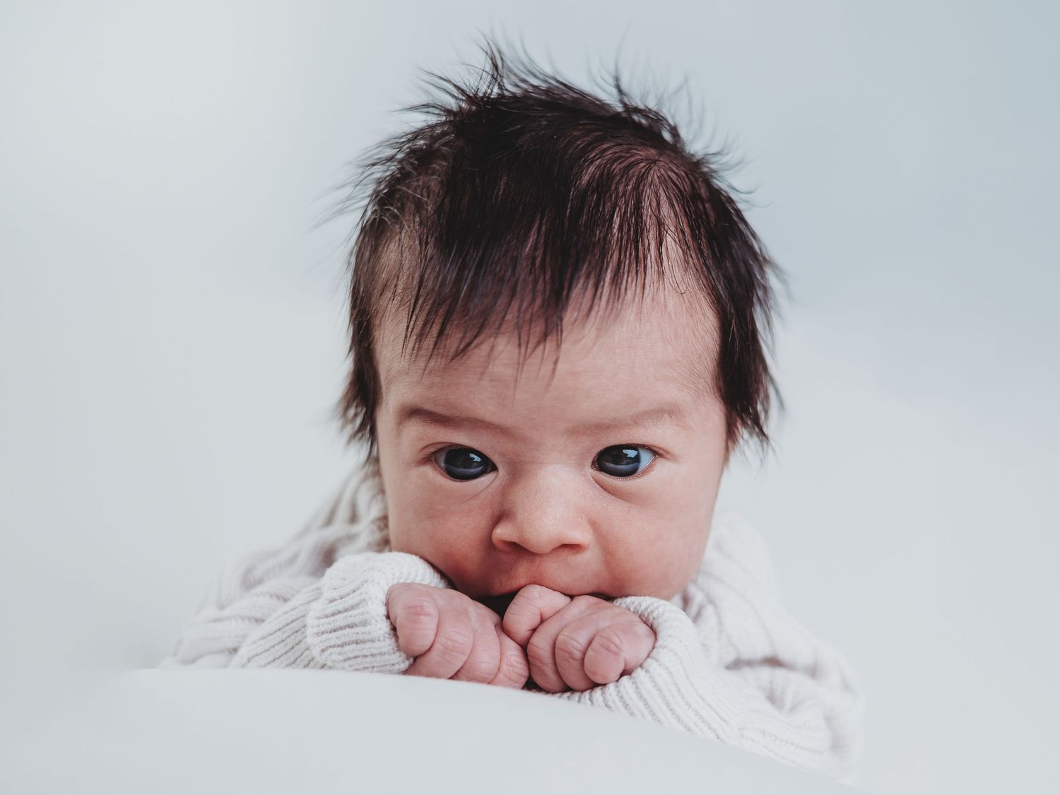 Series of close-up shots showing a baby with dark hair in white clothing.