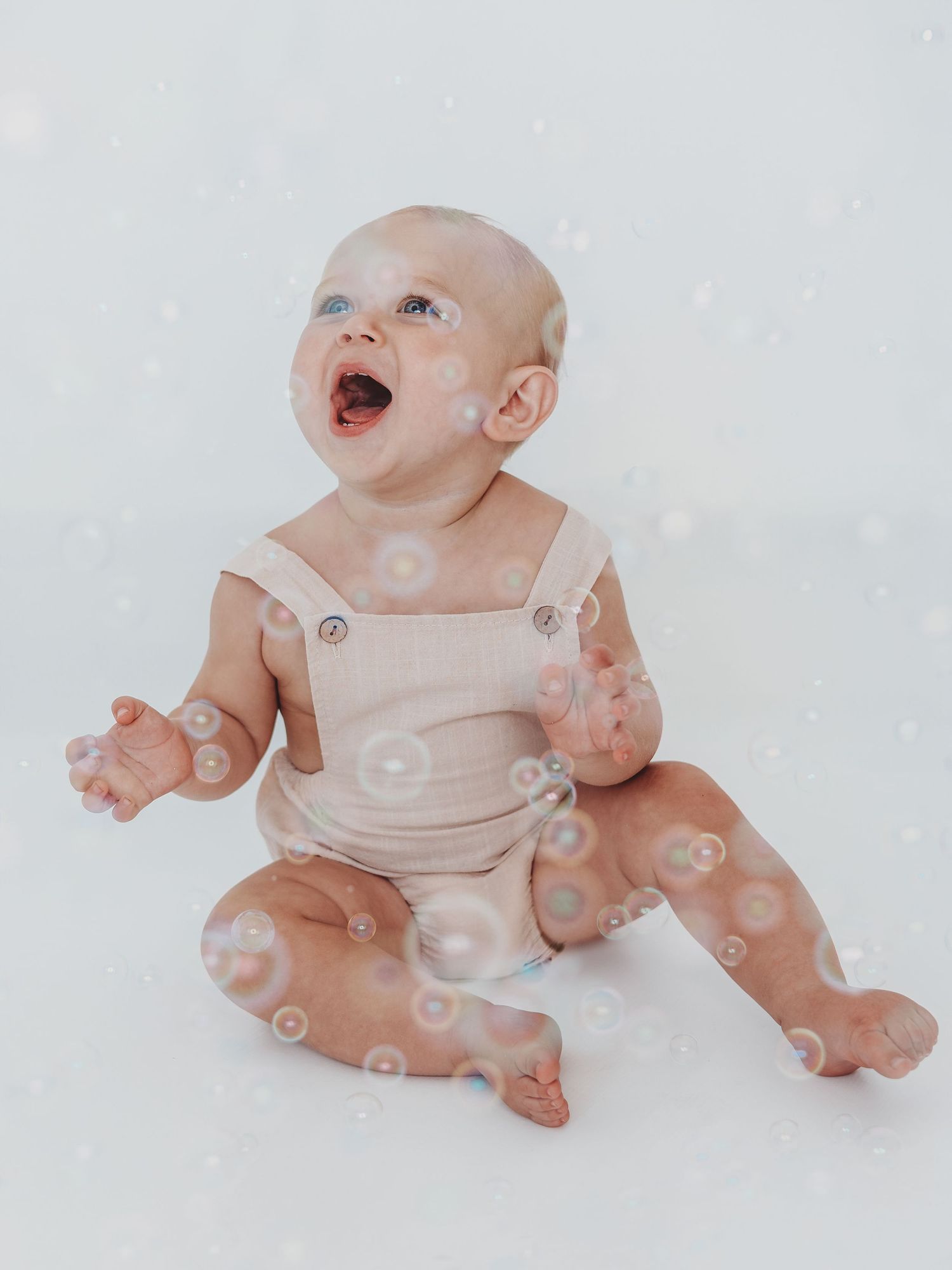 Baby in white onesie playing with soap bubbles while sitting on white background in progressive sequence.