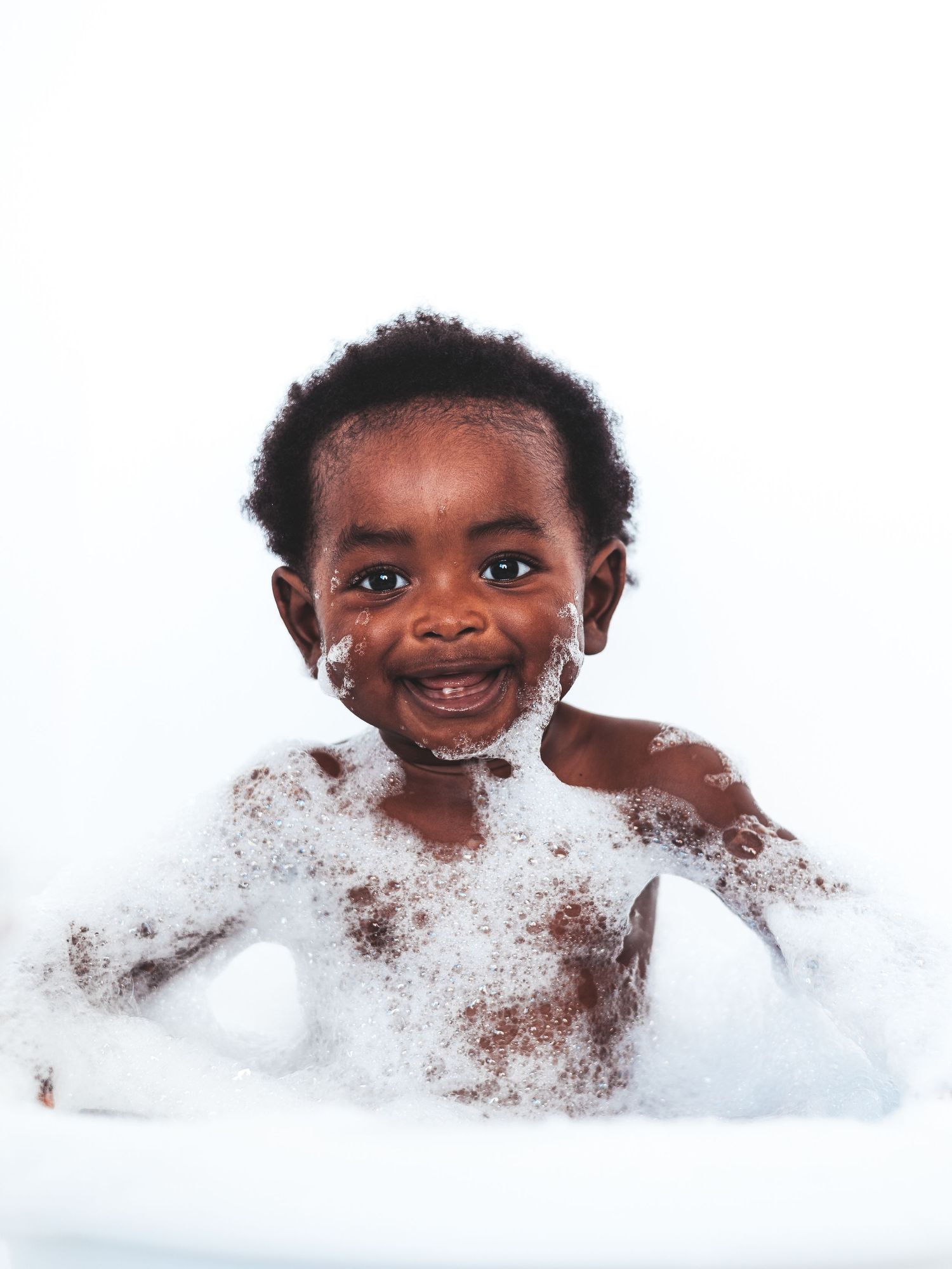 Happy toddler smiling in a bubble bath with soap suds, enjoying bath time.