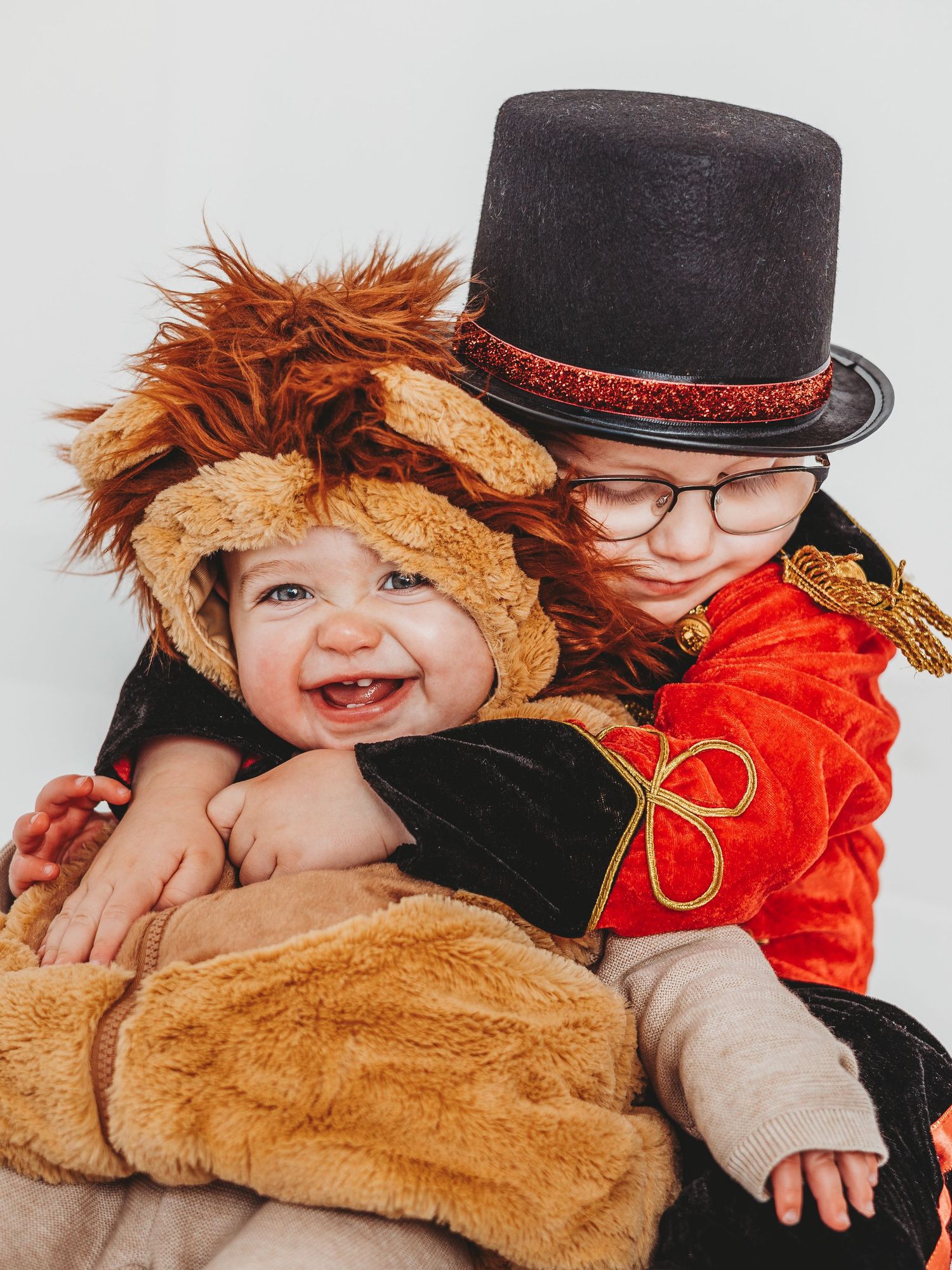 Two babies in Halloween costumes, one as a lion and one as a ringmaster with top hat and glasses.