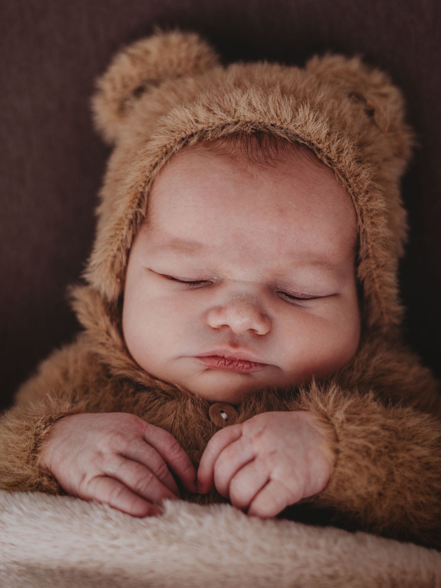 A sleeping baby wearing a cozy brown bear outfit lies peacefully on soft white fabric in a series of connected photos.