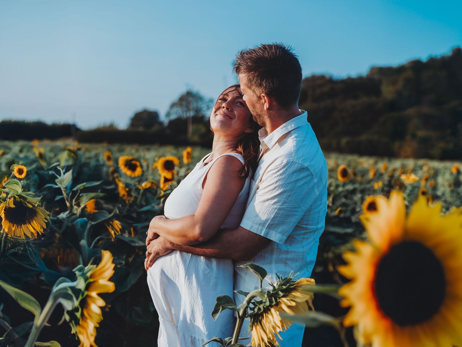 Romantic couple embracing in a sunflower field at sunset. DorsetMaternity and Family Photoshoot. Poole and Bournemouth.